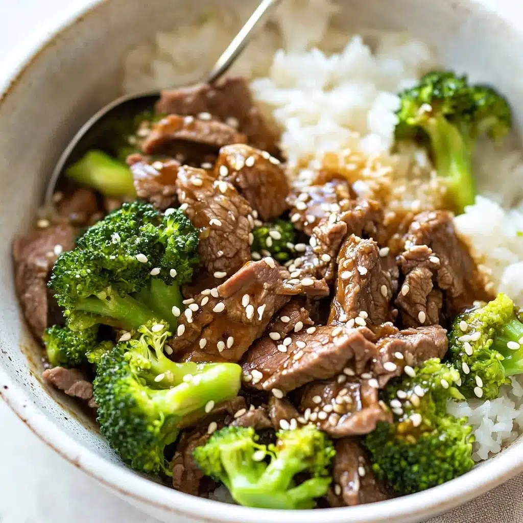 Chinese Beef and Broccoli, Chinese Beef and Broccoli stir-fry, homemade Chinese beef dish, beef and broccoli recipe, quick Chinese takeout dinner A bowl filled with white rice at the bottom, topped with bright green broccoli florets and slices of cooked brown beef mixed with sauce, sprinkled with white sesame seeds. The broccoli pieces are vibrant and fresh-looking, while the beef slices are thin and tender, creating a textured and colorful contrast over the rice. A silver spoon rests inside the bowl, slightly buried in the food. The bowl is white, and it sits on a white marbled surface.
