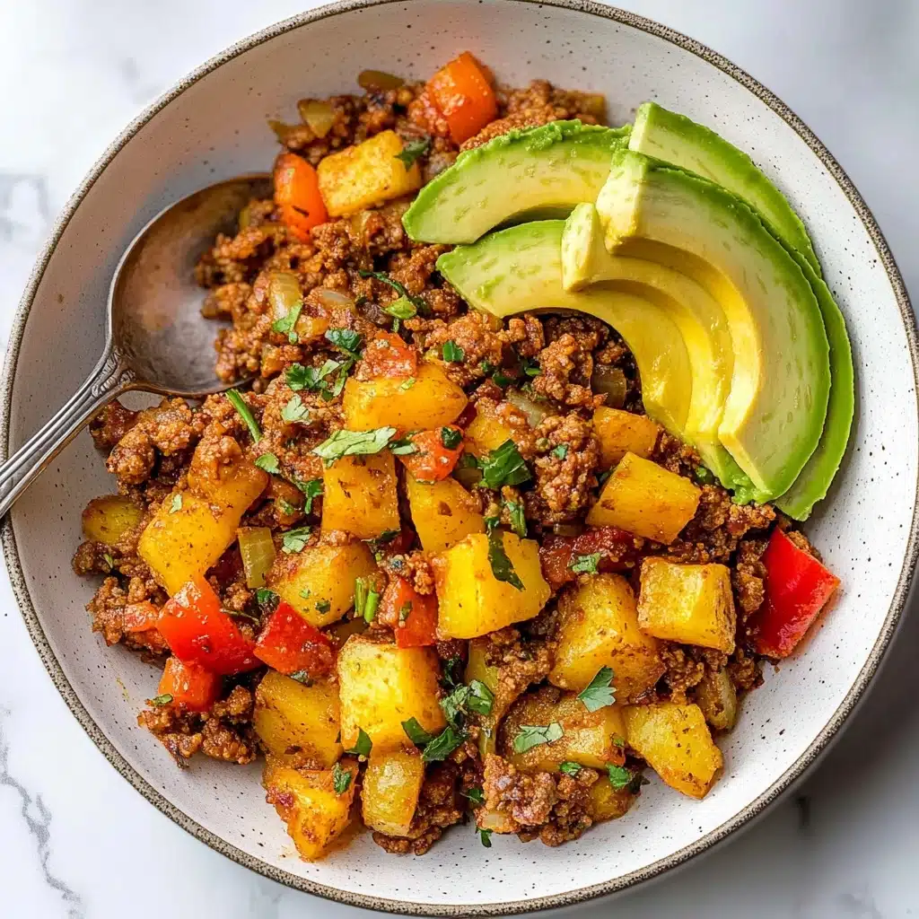 Mexican Ground Beef and Potato Skillet, Mexican beef and potato dish, quick Mexican ground beef skillet, flavorful one-pan Mexican meal, easy Mexican beef skillet A white bowl filled with three main layers of food: the bottom layer has small chunks of browned ground meat mixed with diced cooked yellow potatoes, all seasoned and slightly crispy. The middle layer includes bright red bell pepper pieces and translucent, cooked onion bits scattered throughout. The top layer has three slices of fresh avocado, light green in color, placed on one side of the bowl and sprinkled lightly with green herbs. The bowl is set on a white marbled surface with a silver spoon resting inside the bowl.
