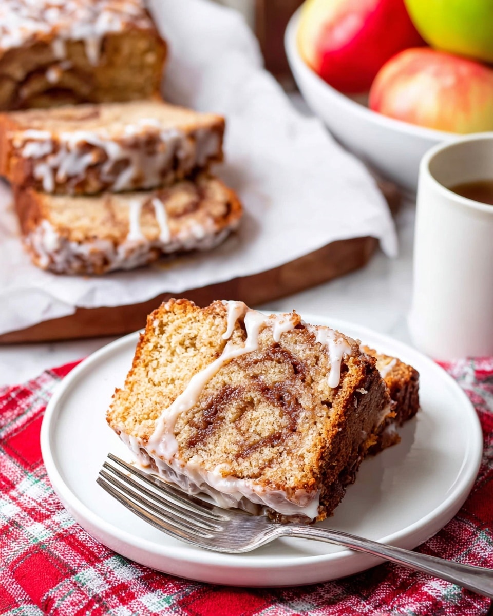 The image shows two thick slices of moist cinnamon swirl bread with a light brown crumb and darker cinnamon layer swirled inside. A white glaze with a shiny, smooth texture covers parts of the slices, dripping down the sides. The slices sit on a white plate with a metal fork beside them. In the background, there is more of the sliced bread with the glaze on white paper and a white bowl of apples on a white marbled surface. A red and white checkered cloth is partly visible below the plate photo taken with an iphone --ar 4:5 --v 7