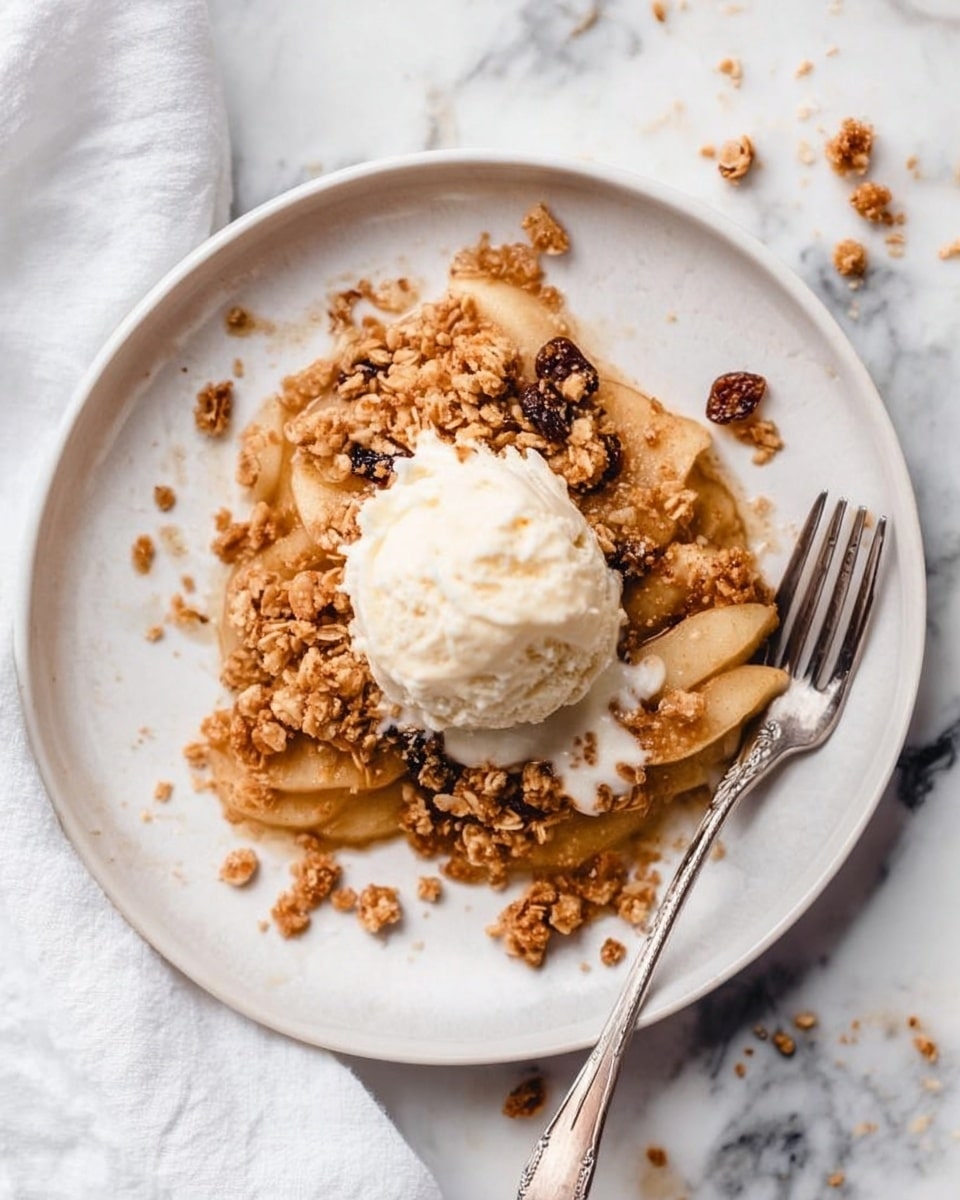A white plate sits on a white marbled surface, holding a dessert with three layers. The bottom layer is made of thin, golden brown apple slices arranged loosely. On top is a crumbly granola layer mixed with raisins, showing a rough texture and warm brown color. A scoop of creamy white vanilla ice cream rests in the center, slightly melting and spreading over the granola and apple layers. A silver fork is placed on the right side of the plate with its handle pointing downwards. Some granola crumbs are scattered around the plate and marble surface. Photo taken with an iphone --ar 4:5 --v 7