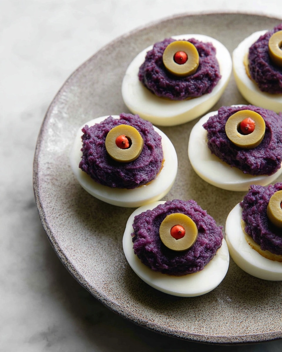 Five halved boiled eggs are arranged on a round white plate with a subtle textured surface. Each egg half has a smooth, firm white base layer. On top of each base is a thick, rough-textured dollop of deep purple filling, creating a rounded mound. At the very top center of each mound is a single green olive slice with a small red pimento inside, adding a pop of color and a smooth circular layer. The whole scene is set against a white marbled textured background. photo taken with an iphone --ar 4:5 --v 7