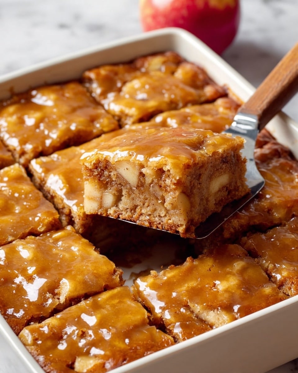 A square piece of golden brown dessert with a slightly shiny top layer is lifted from a tray by a spatula with a light wooden handle, showing a dense, moist inside with bits of nuts scattered throughout. The dessert is cut into multiple square pieces that fit snugly in the silver baking tray. The texture on top looks slightly cracked and caramelized. The background includes a blurred white marbled surface and out-of-focus warm-toned cloth and red fruits. photo taken with an iphone --ar 4:5 --v 7