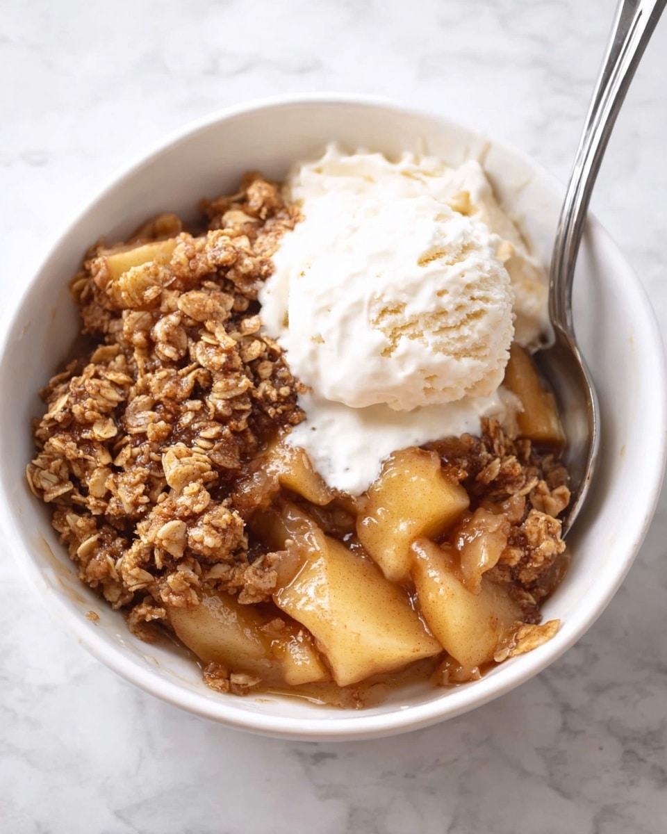 A white bowl filled with warm apple crisp, showing soft, light golden apple chunks at the bottom. On top, there is a thick layer of brown crumbly oat topping with a slightly crunchy look. A scoop of melting white vanilla ice cream sits on the right side, with some ice cream melting into the apple crisp. A silver spoon is placed inside the bowl on the top right side. The bowl is set on a white marbled surface. photo taken with an iphone --ar 4:5 --v 7