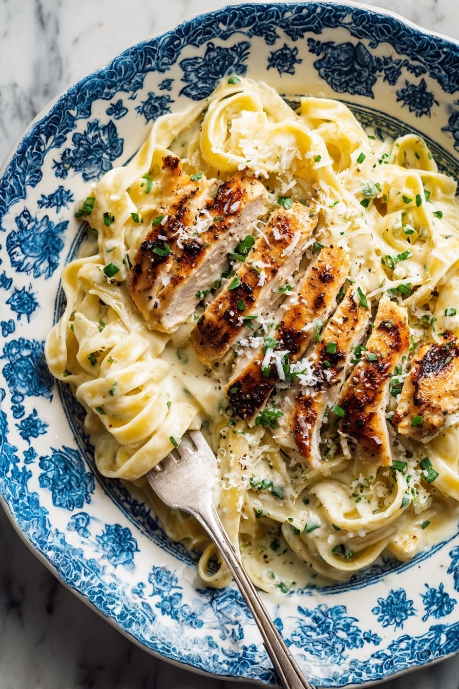 A close-up top view of a white plate with blue patterns filled with three main layers: the bottom layer is creamy, light yellow fettuccine pasta covered in a sauce with a smooth texture; on top of the pasta is a layer of thinly sliced grilled chicken with a golden brown, slightly crisp surface showing grill marks; sprinkled over both pasta and chicken are small pieces of chopped green herbs and finely grated white cheese. A silver fork is stuck into the pasta on the left side of the plate, some pasta twirled around its prongs. The plate sits on a white marbled textured surface. Photo taken with an iphone --ar 2:3 --v 7 - Healthy Chicken Alfredo Greek Yogurt, Healthy Chicken Alfredo, Greek Yogurt Alfredo, Light Chicken Alfredo Recipe, Healthy Pasta with Greek Yogurt