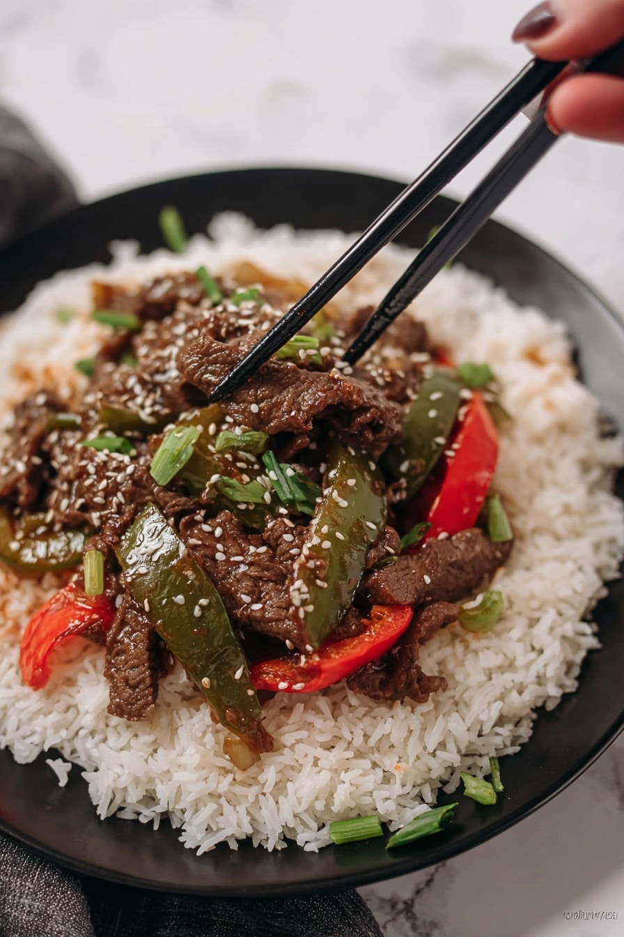 A white plate holds a large base layer of fluffy, long-grain white rice, spread evenly across the plate. On top of the rice sits a colorful stir-fry with three distinct elements: dark brown thin strips of cooked beef, glossy green bell pepper slices, and bright red bell pepper slices. The stir-fry is sprinkled with small white sesame seeds and chopped green onion pieces for freshness. Two black chopsticks rest across the top edge of the plate. The background shows a red bell pepper and green leafy herbs on a white marbled surface. Photo taken with an iphone --ar 2:3 --v 7 - Crockpot Pepper Steak, slow cooker beef stir-fry, Easy Crockpot Beef Recipe, flavorful ground beef dinner, tender crockpot steak
