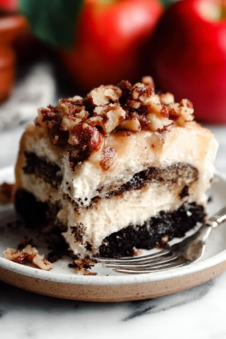 The image shows a close-up of a thick slice of layered dessert on a white plate. The bottom layer is dark and crumbly, looking like crushed chocolate cookies. Above that, there is a creamy, light beige layer that looks soft and smooth. On top, there is a sprinkle of chopped nuts mixed with small crumb pieces, giving a crunchy texture. A metal fork rests on the plate near the dessert. The background has a white marbled surface, and there are whole red apples blurred in the background. Photo taken with an iphone --ar 2:3 --v 7 - Apple Pie Cinnamon Rolls, apple cider caramel sauce, easy cinnamon roll recipe, brunch breakfast ideas, holiday dessert recipes