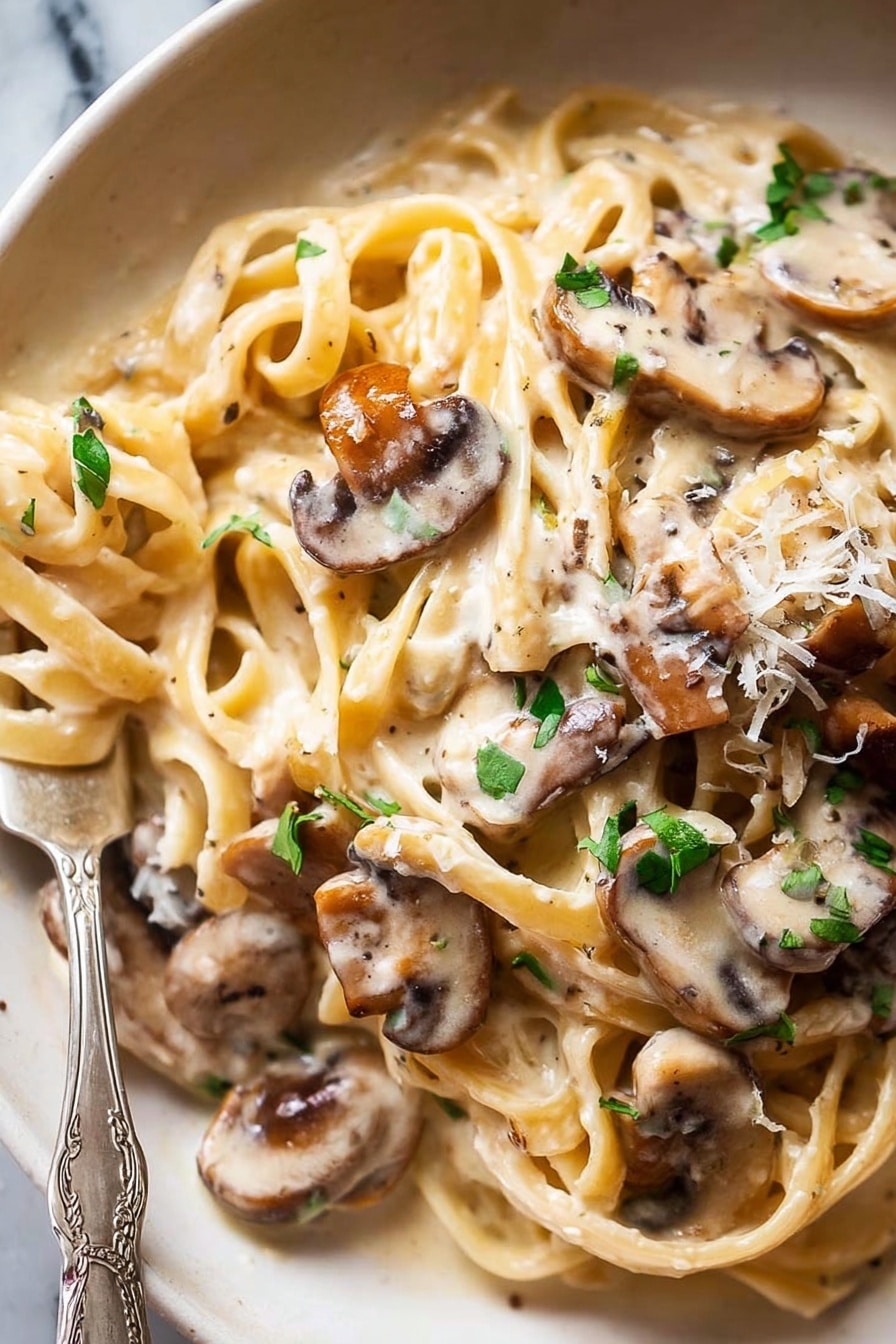 A close-up of creamy pasta with several long, flat noodles twisted and layered, covered in a smooth, off-white sauce. On top and mixed into the pasta are many thin slices of cooked mushrooms with a light brown color and soft texture. Small pieces of fresh green herbs are scattered over the whole dish, adding a splash of color. The dish is on a white plate with a fork partially wrapped in the pasta at the bottom left corner. The background is a white marbled texture. Photo taken with an iphone --ar 2:3 --v 7 - Creamy Mushroom Pasta, mushroom pasta recipe, creamy mushroom pasta dinner, easy mushroom pasta, vegetarian creamy pasta