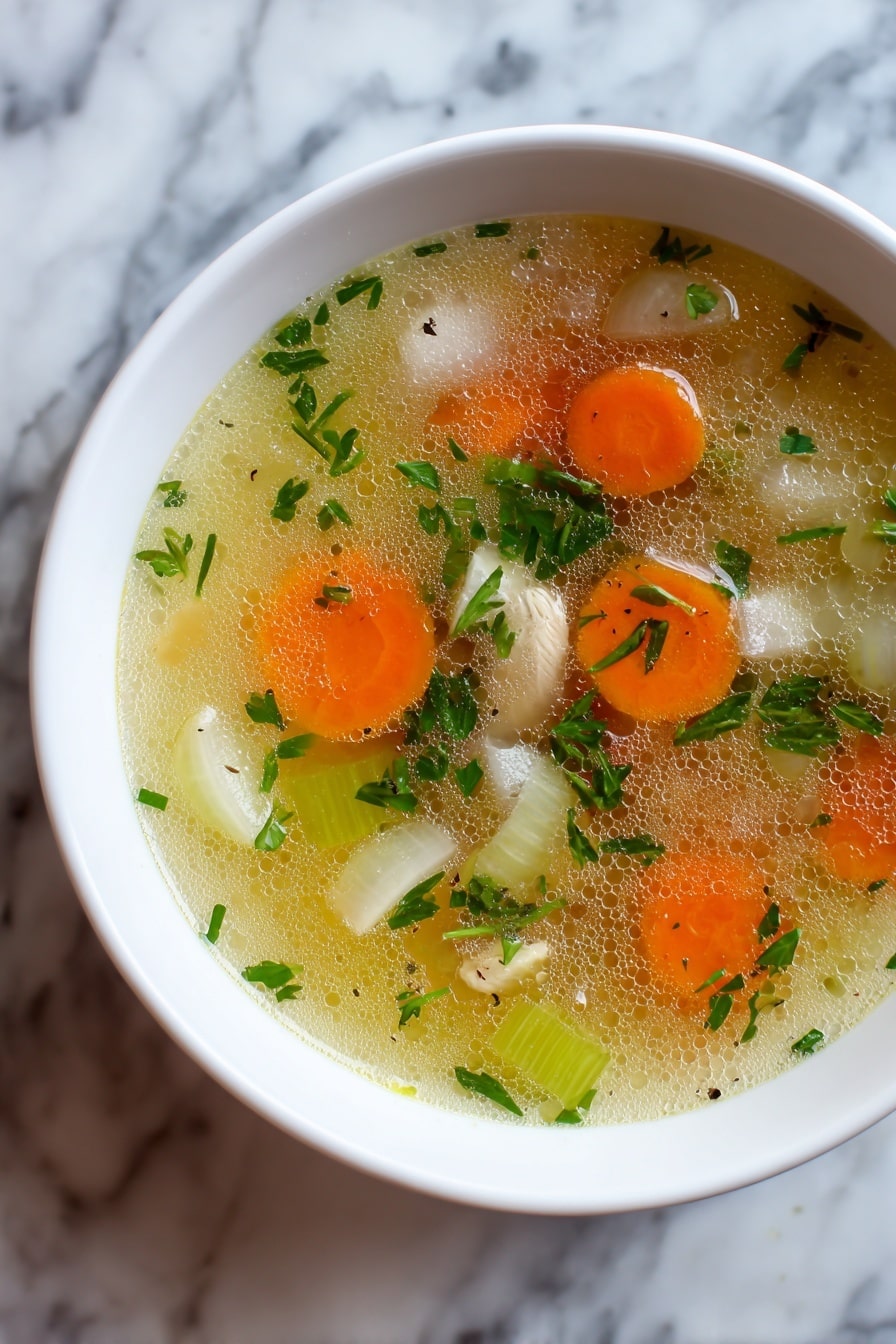 A white bowl filled with clear chicken soup on a white plate, showing three layers: a top layer of clear golden broth with small oil drops, a middle layer with soft shredded chicken pieces in cream color mixed with green leafy vegetables and small orange carrot cubes, and a bottom layer of translucent broth with small green peas and herbs. The bowl is placed on a white marbled surface with a spoon on the right side. Photo taken with an iphone --ar 2:3 --v 7 - Mom's Cold-Season Chicken Soup, comforting chicken soup, homemade chicken broth, easy chicken soup recipe, cold-weather soup