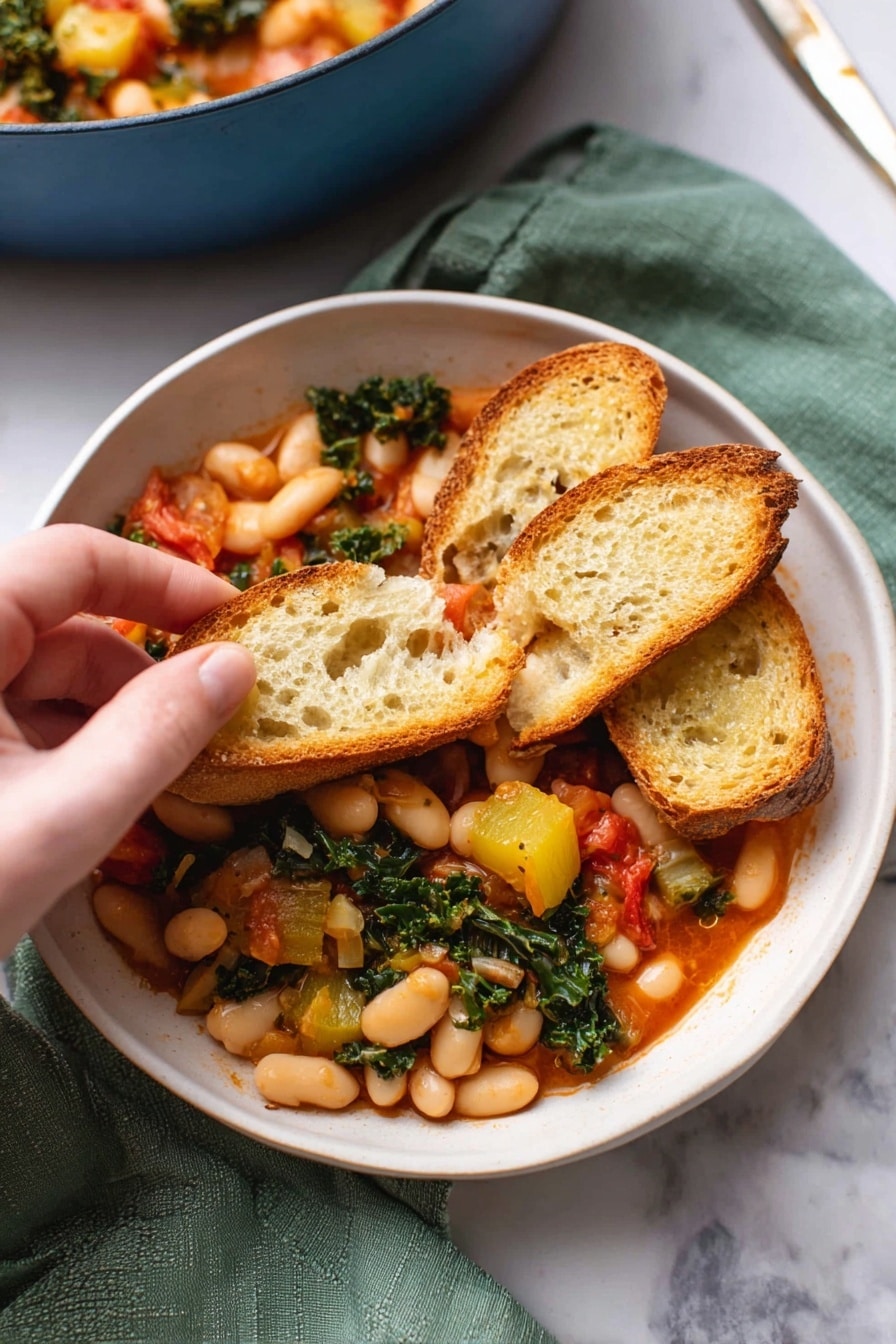 A white bowl filled with a warm stew made of white beans, chunks of yellow squash, wilted green kale, and small red tomato pieces. On top, three slices of toasted baguette bread rest, one slice held by a woman's hand, showing the mix of beans and vegetables piled on it. The stew's sauce is a light red color, and the bread has a golden-brown crust with a porous, soft inside texture. The bowl sits on a green cloth on a white marbled surface, with part of a blue pot filled with more stew blurred in the background. Photo taken with an iphone --ar 2:3 --v 7 - Stewed Great Northern Beans with Kale and Tomatoes, healthy bean stew recipe, hearty vegetable stew, quick vegetarian dinner ideas, comforting bean and greens dish