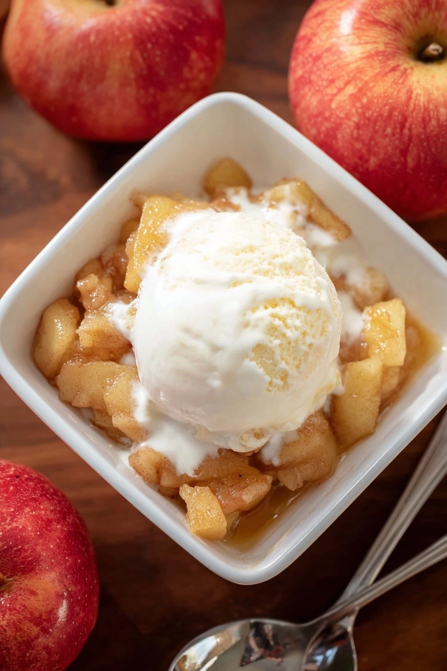 A white square bowl is filled with one layer of soft cooked apple pieces with a light brown color and chunky texture. On top, there is one scoop of creamy white vanilla ice cream that is melting slightly, spreading smooth white cream over the apples. The bowl sits on a wooden surface next to two red apples and a silver spoon. The lighting is soft and natural, highlighting the warm and cool tones of the dessert. photo taken with an iphone --ar 2:3 --v 7 - Apple Brown Betty, apple dessert, fall dessert, easy apple crumble, cinnamon apple crisp