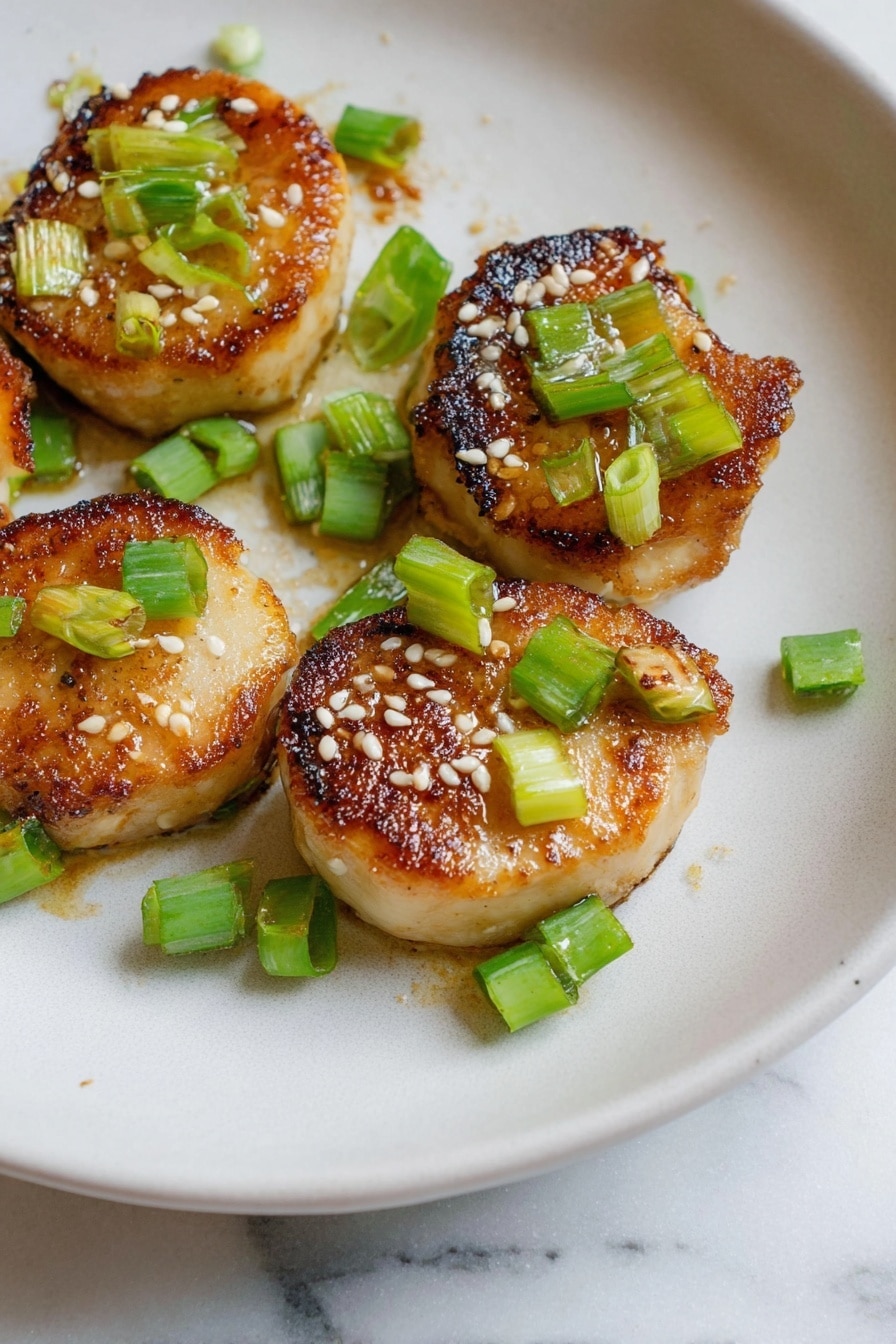 The image shows five small round pieces of golden-brown cooked food with a slightly crispy and caramelized texture on top. Each piece is garnished with small green chopped scallions and sprinkled with white sesame seeds. They are arranged on a white plate with a smooth, slightly matte surface, placed on a white marbled textured background. The food looks warm and freshly cooked, with the colors of golden brown, light green, and white creating a fresh and appetizing look. photo taken with an iphone --ar 2:3 --v 7 - Miso Soy King Oyster Mushroom, Vegan Scallops, Plant-Based Seafood, Easy Vegan Dinner, Umami Mushroom Recipes