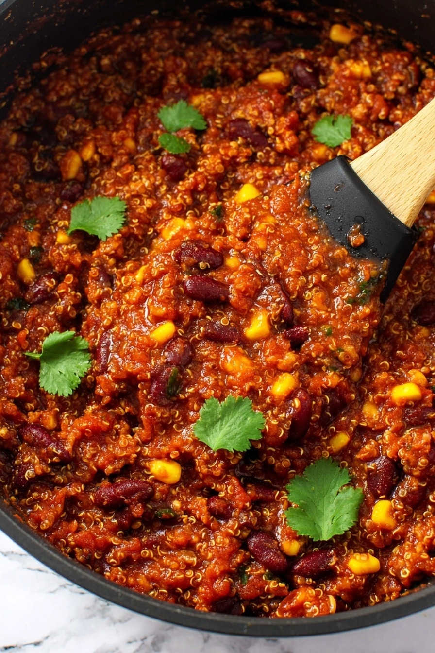 The image shows a thick, rich mixture in a black pan filled with three main layers: grains that look like tiny beige quinoa, dark red kidney beans, and bright yellow corn kernels, all mixed with a deep red tomato-based sauce. The texture is chunky with small bits of vegetables and beans visible throughout. There are several fresh green cilantro leaves scattered on top for contrast. A wooden spoon with a black silicone head is scooping some of the mixture from the pan. The background is a white marbled texture. Photo taken with an iphone --ar 2:3 --v 7 - Slow Cooker Vegan Bean & Quinoa Chili, vegan chili, healthy vegan dinner, hearty plant-based chili, easy vegan slow cooker meal