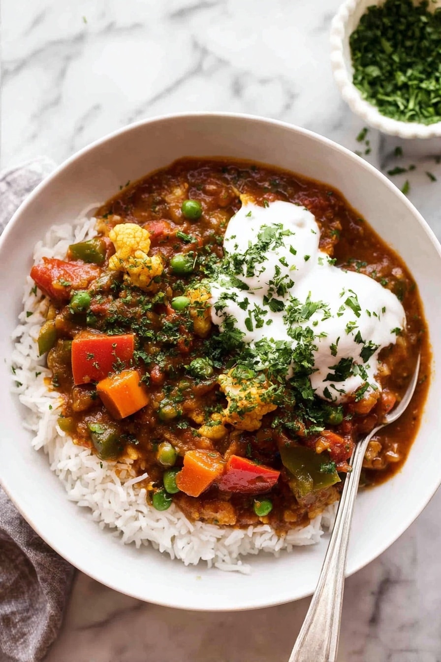 A white bowl filled with a base layer of white rice topped with a colorful vegetable curry. The curry has pieces of orange carrots, bright green peas, red bell peppers, and bits of cauliflower all mixed in a rich reddish-brown sauce. On top of the curry, there are two dollops of smooth white yogurt sprinkled with chopped green herbs. A silver spoon rests inside the bowl on the right side. The bowl is placed on a white marbled surface, and in the background, there is a small white bowl filled with chopped green herbs. photo taken with an iphone --ar 2:3 --v 7 - Vegetable Curry, easy vegetable curry, hearty vegetable curry recipe, vegan curry bowl, cozy Indian vegetable curry