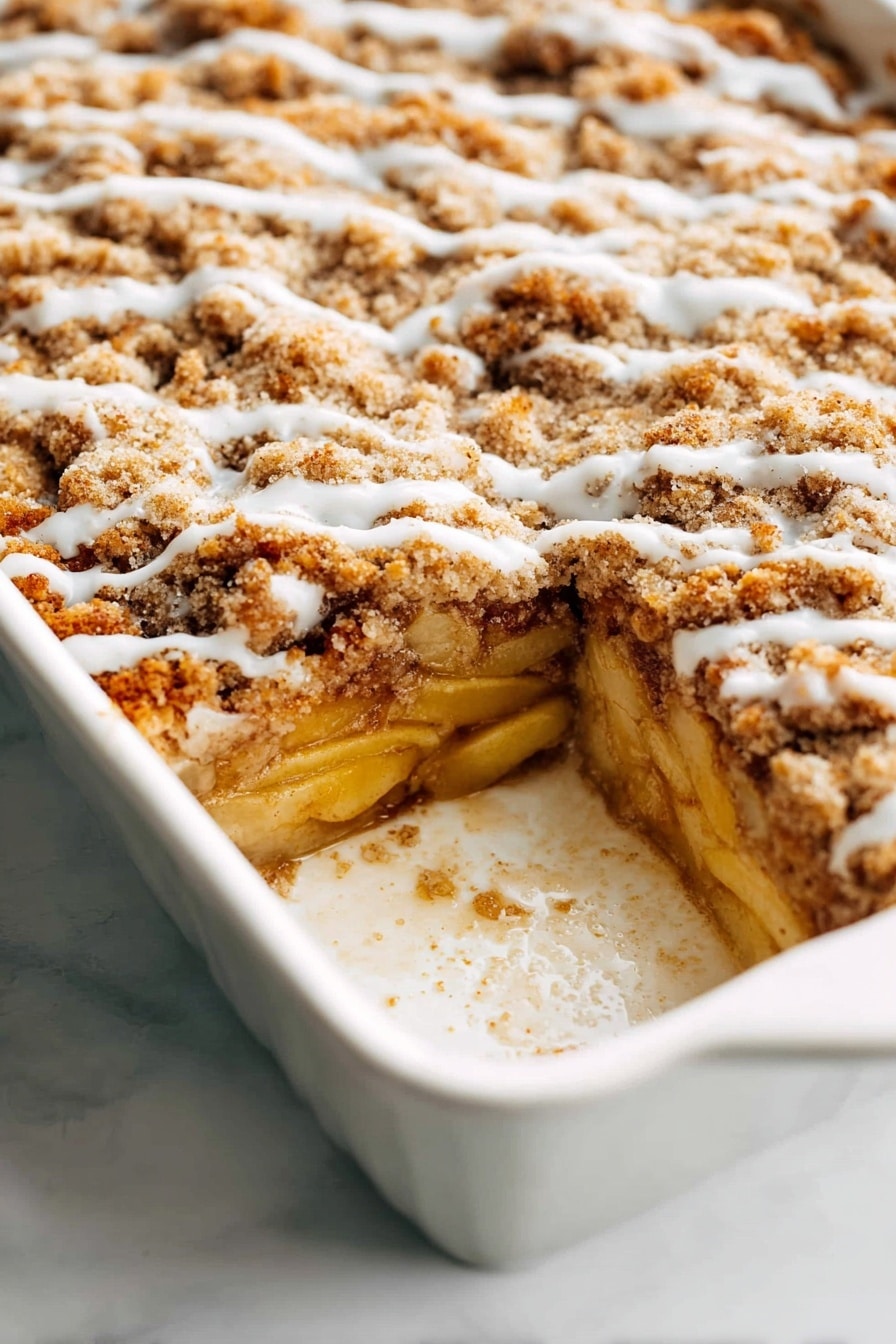 A white baking dish holds a multi-layered baked dessert with three visible layers. The bottom layer is made of soft cooked apple slices, pale yellow in color, resting on a thin, golden crust. Above this, there is a thick, light brown crumbly streusel layer that looks crunchy and uneven, covering the apples. A thin, slightly shiny drizzle of white icing runs lightly across the top streusel layer in wavy lines. The edges of the dish show some baked-on residue, adding a homemade feel. The white marbled surface beneath the dish adds a clean, bright background. photo taken with an iphone --ar 2:3 --v 7 - Apple French Toast Casserole, apple cinnamon breakfast, easy baked french toast, cozy brunch dish, apple dessert casserole