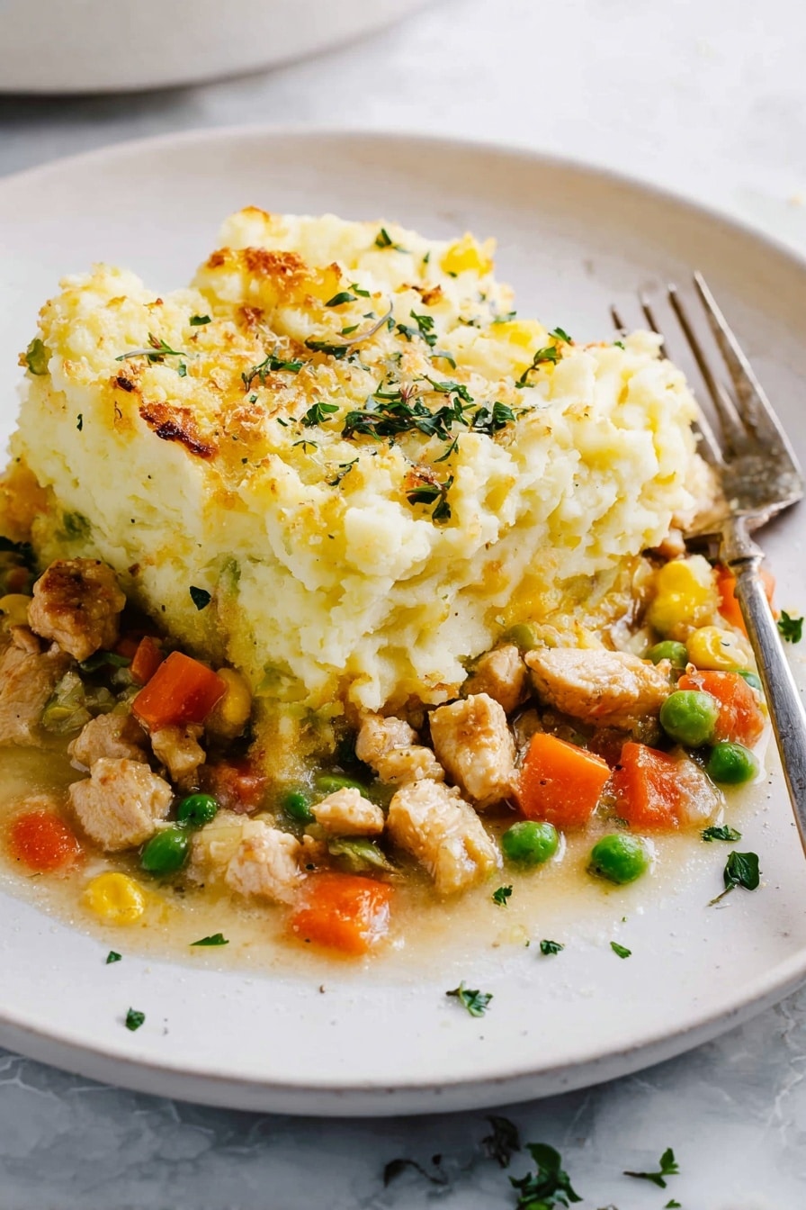 The dish shows two layers on a white plate with a white marbled surface below. The bottom layer is a mix of small pieces of light brown cooked chicken, bright orange carrot cubes, green peas, and some yellow bits, all in a light sauce. The top layer is a thick, fluffy heap of mashed potatoes with a pale yellow color and a slightly browned, baked texture on the edges. Small green herb pieces are sprinkled over the top and around the plate. A metal fork rests on the right side of the plate. photo taken with an iphone --ar 2:3 --v 7 - Healthy Turkey Shepherd's Pie, healthy shepherd's pie with turkey, nutritious turkey meat pie, low-fat turkey shepherd's pie, healthy comfort food recipes