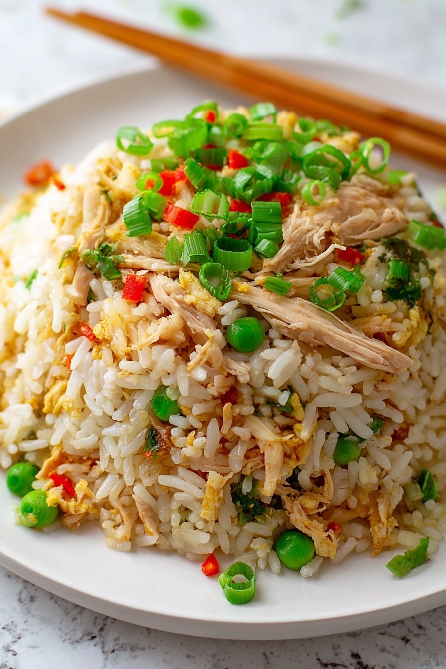 A close-up view of a mound of fried rice on a white plate, placed on a white marbled surface. The dish has three main layers: the bottom layer is white and slightly golden rice grains, the middle layer contains shredded light brown chicken pieces mixed with small green peas, and the top layer is scattered with bright green chopped spring onions and tiny red bell pepper bits. Wooden chopsticks rest diagonally at the back of the plate. Photo taken with an iphone --ar 2:3 --v 7 - Easy Chicken Fried Rice, quick chicken fried rice, homemade fried rice recipe, simple stir-fry chicken and rice, delicious chicken fried rice