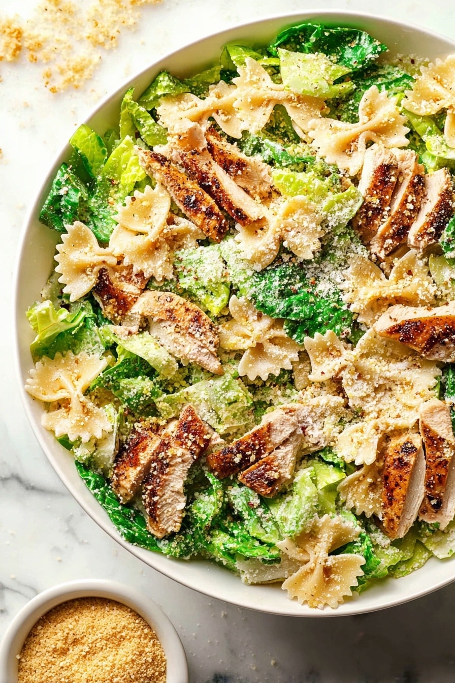 A large white bowl filled with a colorful salad showing layers of light green leafy lettuce pieces mixed with beige farfalle pasta shapes. On top of this are slices of browned, cooked chicken that have a slightly crispy texture. The dish is sprinkled with light brown grated cheese and breadcrumbs, giving a crumbly look over the salad. The bright green lettuce pieces and the pasta form the base layer, with chicken pieces scattered evenly above. The white marbled surface underneath adds a clean look, and there is a small bowl of extra breadcrumbs on the side. photo taken with an iphone --ar 2:3 --v 7 - Creamy Chicken Caesar Pasta Salad, chicken Caesar pasta salad, easy pasta salad recipes, summer pasta salad, crowd-pleasing pasta salad