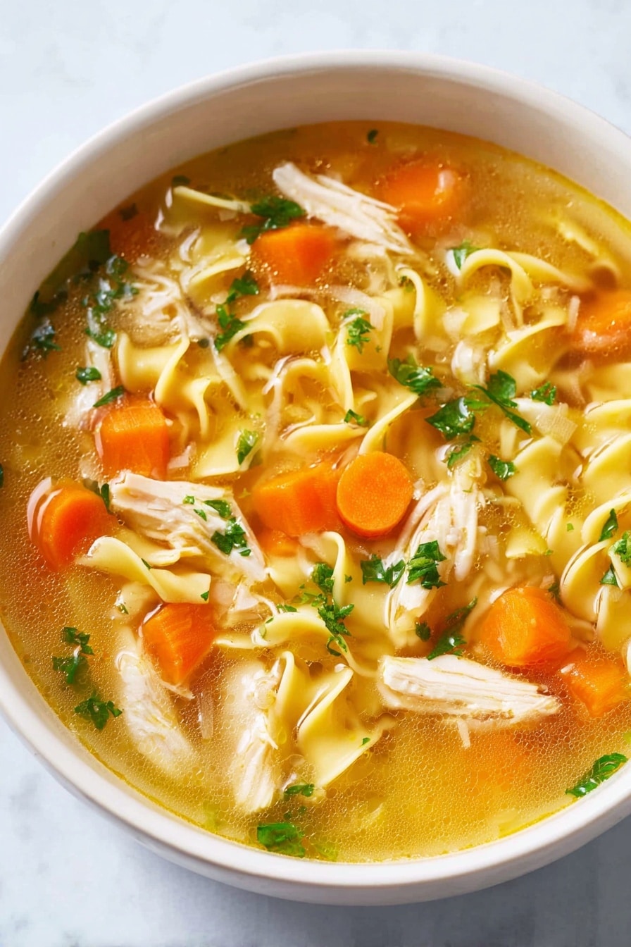 A white bowl filled with clear golden broth containing curly yellow noodles, bright orange carrot cubes, soft white onion pieces, light beige shredded chicken, and small green parsley leaves scattered on top, all resting on a white marbled surface photo taken with an iphone --ar 2:3 --v 7 - Homemade Chicken Noodle Soup, chicken noodle soup recipe, comforting chicken soup, easy homemade chicken soup, cozy chicken noodle soup