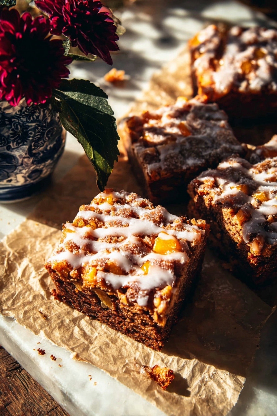 The image shows three thick square slices of a baked dessert with a dark brown base full of small orange chunks inside, topped with a light drizzle of white glaze that has a shiny and smooth texture. The dessert slices sit on crinkled parchment paper with some scattered crumbs around. To the top left, there is a small blue and white vase holding a dark red flower with deep green leaves. The whole scene is lit by warm sunlight creating strong shadows and highlights, placed on a white marbled surface photo taken with an iphone --ar 2:3 --v 7 - Glazed Honeycrisp Apple Fritter Cake, apple fritter cake recipe, easy apple cake with glaze, fall dessert recipes, homemade apple cake