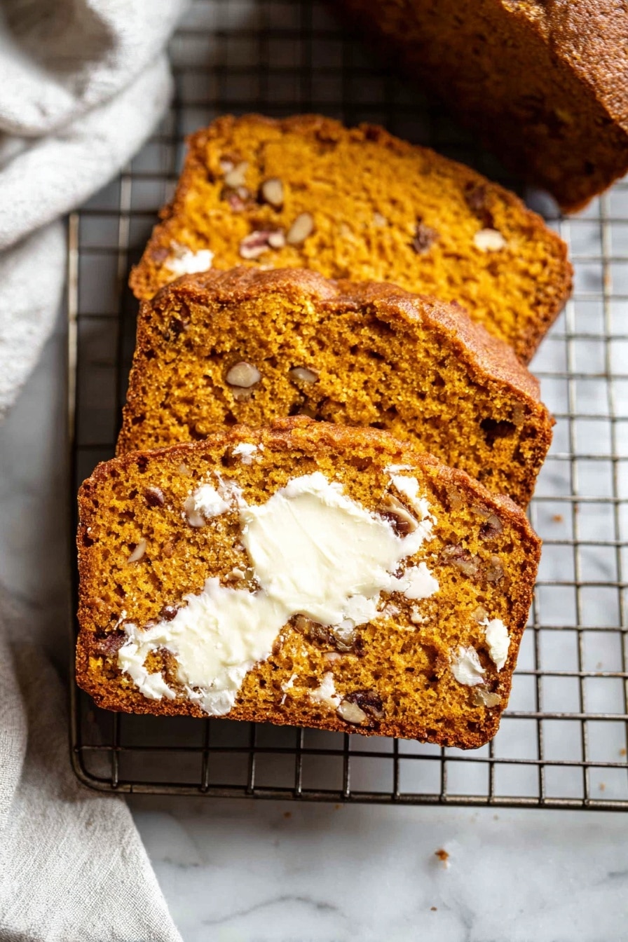 The image shows three thick slices of moist, orange-brown bread with small pieces of nuts inside, laid out on a metal cooling rack. The front slice is spread with melting white butter that contrasts with the bread’s warm color, showing a soft and slightly crumbly texture. The nuts inside the bread add darker brown spots throughout. The cooling rack is placed on a white marbled surface, and part of a white cloth is visible in the background. photo taken with an iphone --ar 2:3 --v 7 - Easy Pumpkin Bread, pumpkin bread recipe, fall baking ideas, moist pumpkin bread, cozy pumpkin bread