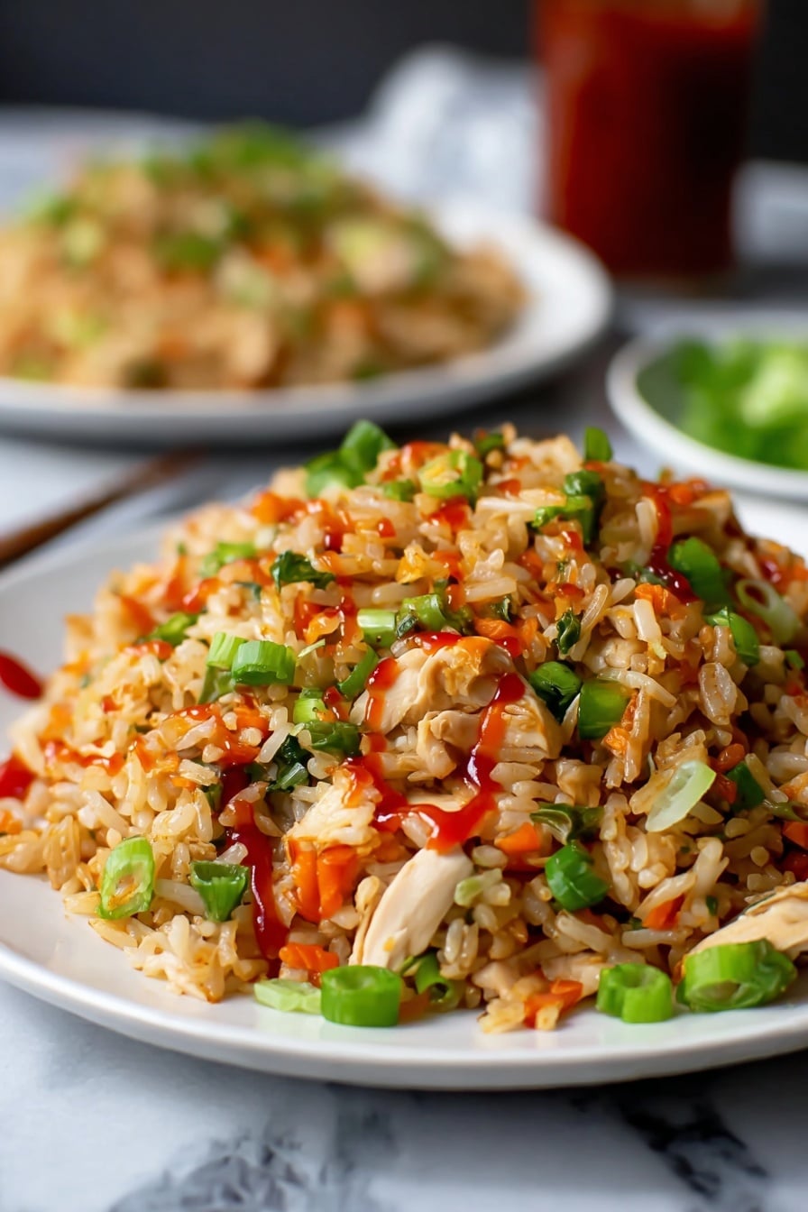 A close-up view of a white plate filled with fried rice, showing layers of light brown rice mixed with small pieces of white chicken, bright green chopped spring onions, and small orange-red peppers scattered throughout. The rice is lightly coated with red sauce drizzled on top, adding a glossy texture. In the background, there is a blurred white plate with more fried rice, placed on a white marbled surface. The overall colors are warm with green, red, and white contrasts. Photo taken with an iphone --ar 2:3 --v 7 - Easy Chicken Fried Rice, quick chicken fried rice, homemade fried rice recipe, simple stir-fry chicken and rice, delicious chicken fried rice