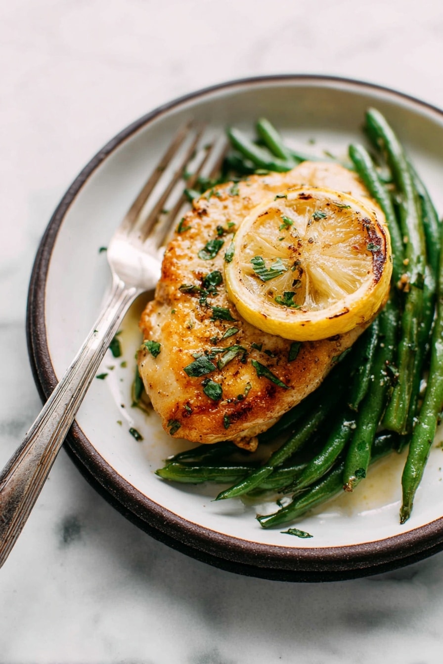 The image shows a single piece of golden-brown cooked chicken placed on top of a bed of green beans. Under the chicken, there is a slice of grilled lemon adding a pop of yellow color. The chicken is sprinkled with fresh green herbs and some seasoning that gives it a slightly glossy texture. The dish is served on a white plate with a dark rim, and a silver fork with an aged handle is resting on the edge of the plate. The surface beneath the plate has a white marbled texture, creating a clean and simple background. photo taken with an iphone --ar 2:3 --v 7 - Garlic Lemon Butter Chicken Skillet, easy chicken skillet recipe, lemon butter chicken, one-pan chicken dinner, flavorful chicken recipes