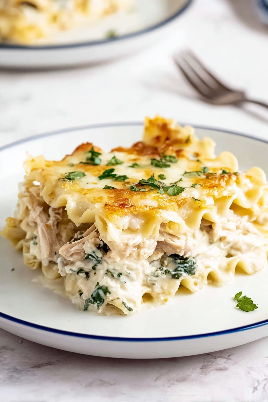 A single piece of lasagna is placed on a white plate with a thin blue rim, showing about four layers. The top layer is light golden with melted cheese and small green parsley flakes scattered on it. Below that is a creamy white sauce mixed with green spinach leaves and chunks of light brown cooked chicken. The pasta layers are soft and wavy, pale yellow in color, separating the cheesy and vegetable layers. The plate is on a white marbled surface with a blurred second plate and a fork in the background. Photo taken with an iphone --ar 2:3 --v 7 - Creamy Chicken Alfredo Lasagna, Chicken Alfredo lasagna, Creamy lasagna with chicken, Easy chicken lasagna recipe, Gourmet chicken Alfredo dish