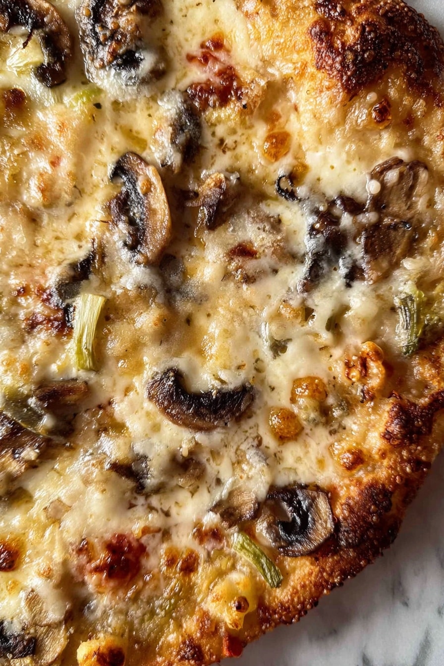 A close-up view of a pizza showing one visible layer with melted cheese covering the surface in creamy white and light golden shades, dotted with browned spots. There are slices of browned mushrooms scattered unevenly across the pizza, adding dark brown and black shapes. Small pieces of slightly green and white vegetables are distributed between the mushrooms and cheese, with some reddish tomato bits peeking through. The edges show a browned crust with some darker burnt spots. The pizza is on a white marbled surface. photo taken with an iphone --ar 2:3 --v 7 - Chicken Zucchini Bake, healthy chicken casserole, easy zucchini bake, protein-packed veggie bake, light comfort food