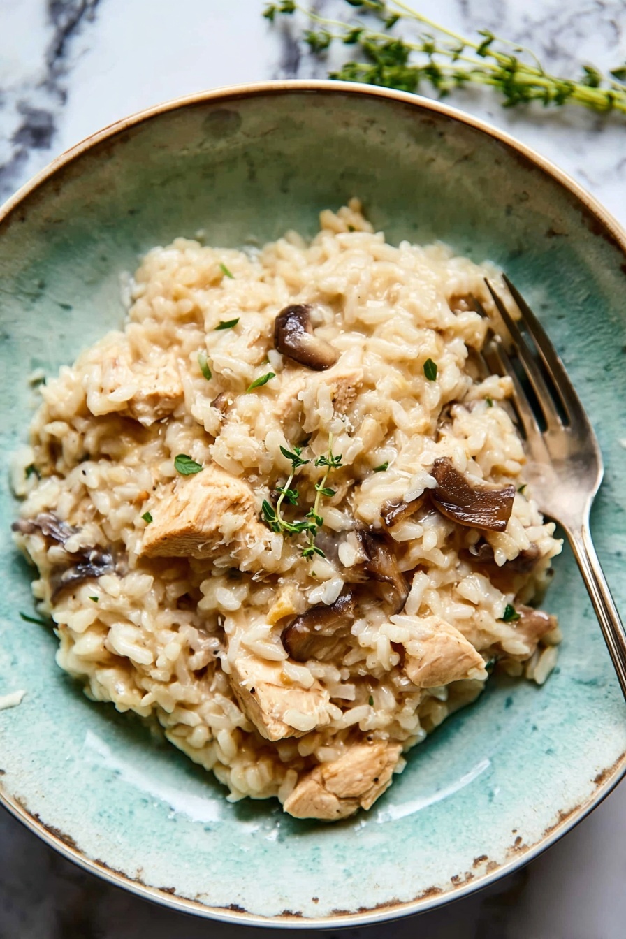 A textured turquoise bowl filled with creamy light beige risotto as the base layer, mixed with medium brown whole mushrooms and light tan chunks of chicken scattered evenly on top. A few sprigs of fresh green herbs sit on one side, adding a pop of color. The bowl rests on a white marbled surface with a folded dark grey cloth nearby, and a silver fork placed inside the bowl on the right side. The overall look is soft and earthy, with natural lighting enhancing the creamy texture of the dish photo taken with an iphone --ar 2:3 --v 7 - Chicken Mushroom Risotto with Thyme, creamy chicken mushroom risotto, easy mushroom risotto recipe, comforting weeknight risotto, thyme flavored risotto