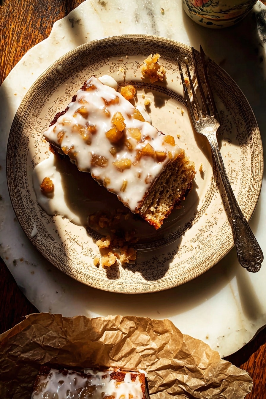 A beige patterned plate holds a rectangular piece of dessert with a rough brown base layer filled with small golden-brown chunks. The top layer is covered in a thick white glaze dripping down the sides and pooling slightly on the plate. There are small scattered bits of the dessert around the main piece, and an old-fashioned silver fork rests diagonally across the plate, partially touching the dessert. The plate sits on a white marbled surface, with sunlight casting strong shadows. A portion of the dessert is also on crumpled brown paper at the bottom of the image, also drizzled with white glaze. Photo taken with an iphone --ar 2:3 --v 7 - Glazed Honeycrisp Apple Fritter Cake, apple fritter cake recipe, easy apple cake with glaze, fall dessert recipes, homemade apple cake