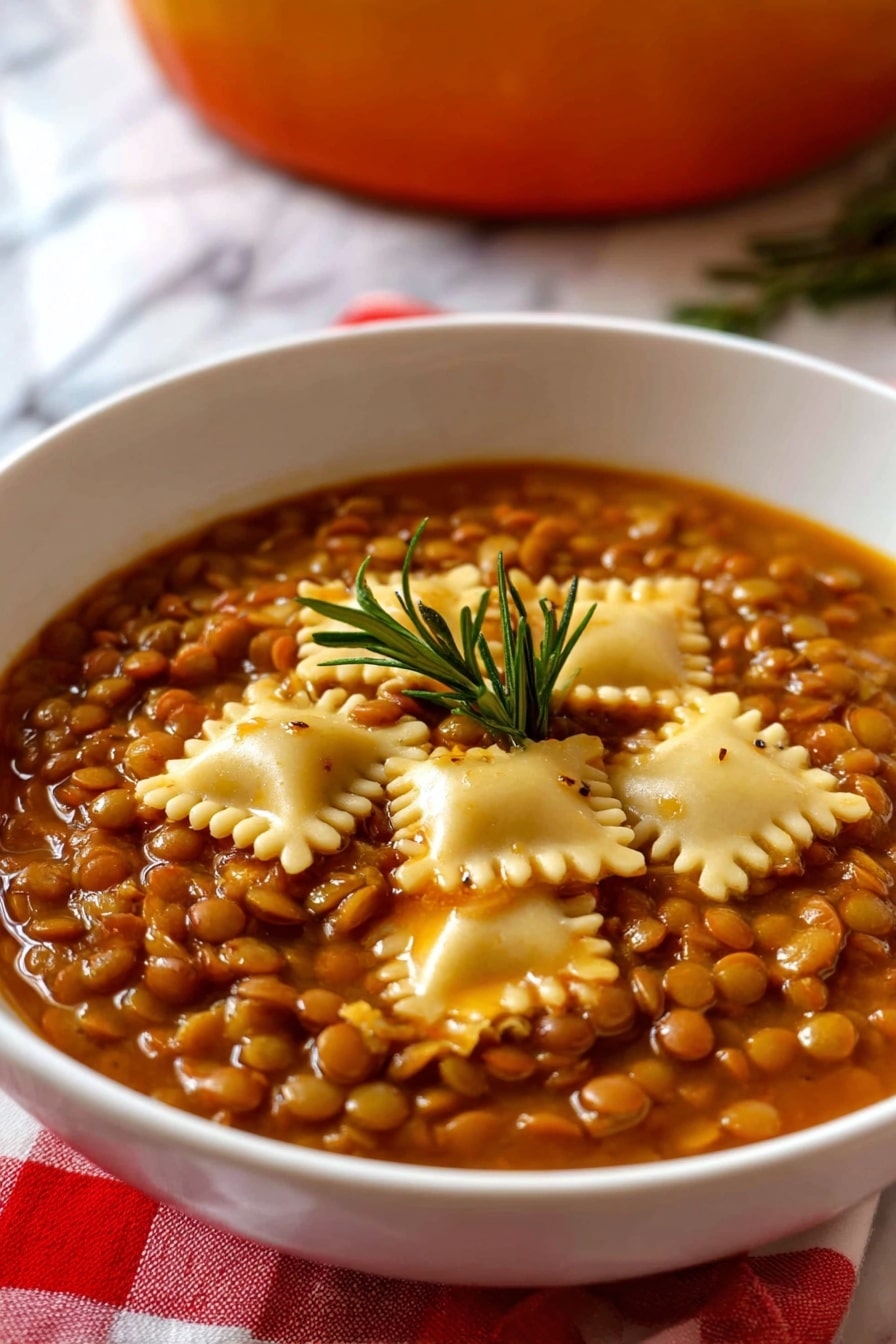 The image shows a white bowl filled with a thick vegetarian lentil soup layered with small, round brown lentils covering the entire surface, mixed with several square pieces of pale yellow pasta scattered evenly on top. The soup has a rich, brownish-orange broth giving the dish a warm color, with a small green rosemary sprig placed in the center as a garnish. The bowl rests on a red and white checkered cloth with a white marbled surface below, and a blurred background hinting at an orange pot. Photo taken with an iphone --ar 2:3 --v 7 - Umbrian Lentil Soup with Pasta, Umbrian Lentil Soup, Italian Lentil Soup, hearty lentil and pasta soup, traditional Italian lentil dish