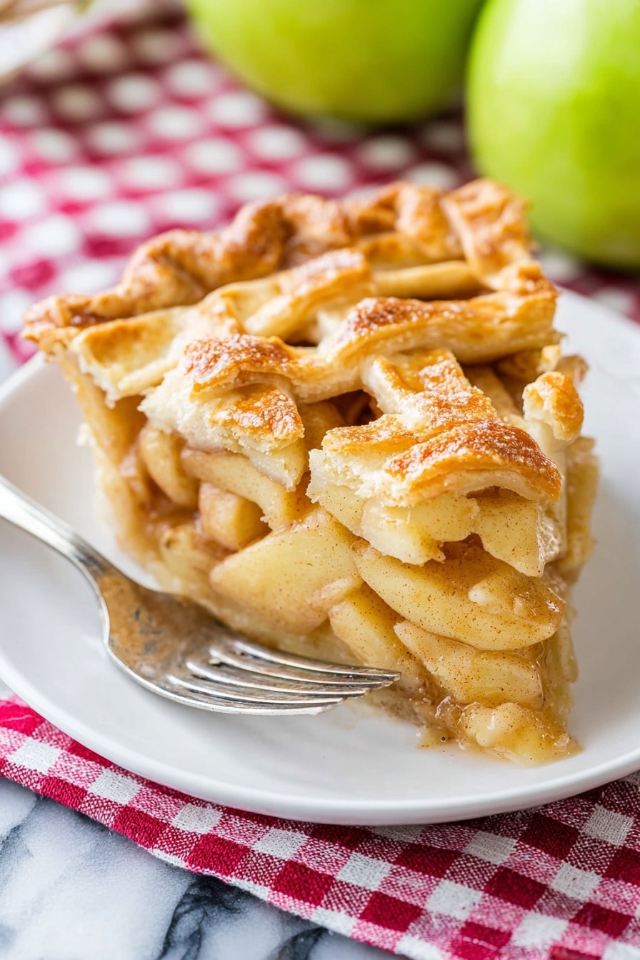 A piece of apple pie sits on a white plate with a silver fork resting beside it. The pie has a golden-brown lattice crust on top, with visible layers of soft, spiced apple slices underneath that appear juicy and tender. The crust edges are slightly crimped and have a flaky texture. Behind the pie, there are two green apples slightly out of focus. The plate is placed on a red and white checkered cloth, all set on a white marbled surface. Photo taken with an iphone --ar 2:3 --v 7 - Apple Pie, best apple pie, homemade apple pie, classic apple pie, easy apple pie