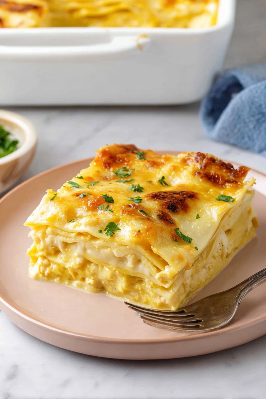 A square piece of lasagna with three visible layers is placed on a pale pink plate on a white marbled surface. The top layer is covered with melted golden-yellow cheese, sprinkled with fresh green herbs. Beneath, you can see creamy yellow sauce mixed with soft white pasta sheets and some herbs. In the background, a white baking dish with a golden top edge of more lasagna and a silver fork resting on the plate accompany the serving. photo taken with an iphone --ar 2:3 --v 7 - Butternut Squash Lasagna, butternut squash lasagna recipe, fall vegetarian lasagna, creamy healthy lasagna, cozy seasonal lasagna