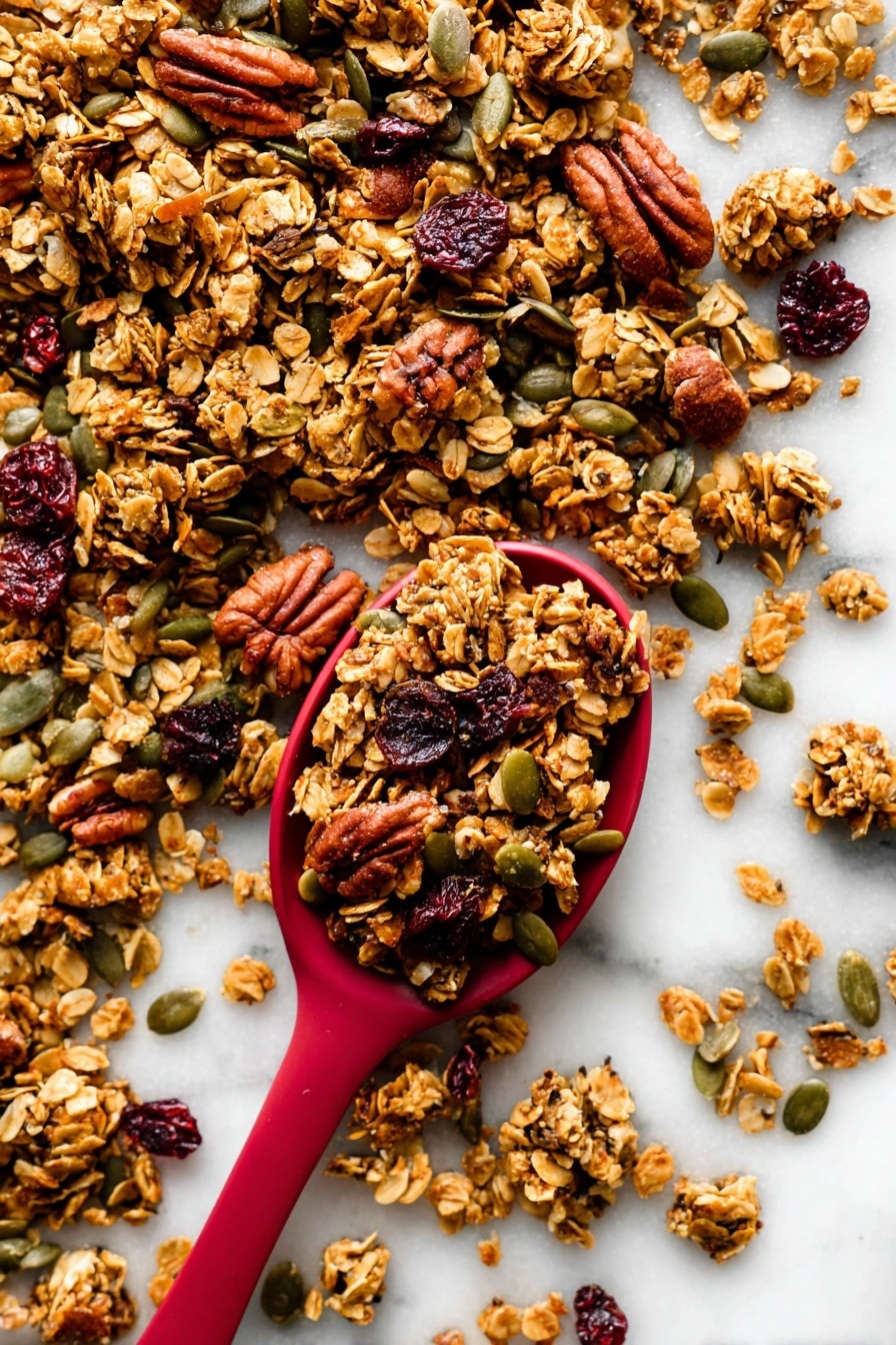 The image shows a close-up of crunchy granola scattered on a white marbled surface with a red spoon filled with granola placed near the center. The granola is made of golden-brown toasted oat clusters mixed with darker brown pecans, green pumpkin seeds, and dark red dried cranberries. The textures vary from rough and chunky oats and nuts to smooth seeds, creating a rich and inviting look. The red spoon contrasts strongly with the white background and the natural colors of the granola around it. photo taken with an iphone --ar 2:3 --v 7 - Pumpkin Spice Granola with Cranberries, fall breakfast ideas, healthy breakfast recipes, homemade granola, cozy autumn treats