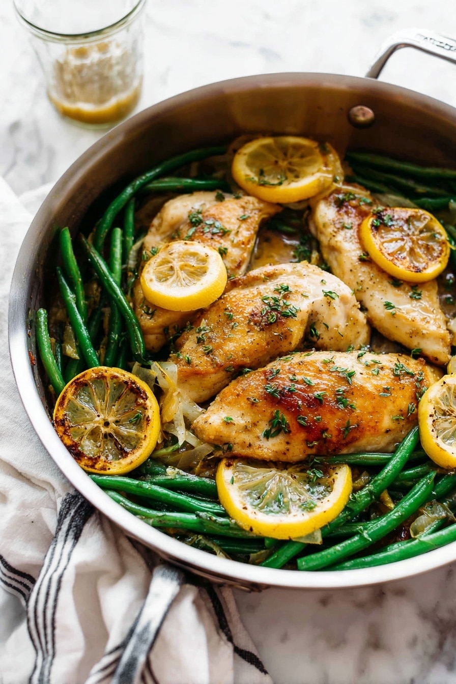 A round silver pan holds a dish with three light golden brown cooked chicken pieces on top. Underneath and around the chicken are bright green beans and several round slices of cooked lemon that are golden and slightly charred on the edges. The chicken is sprinkled with small green herb pieces and has a slightly shiny sauce coating parts of it. The pan is placed on a white marbled surface, with a white cloth with black stripes in the back left and a glass cup with some sauce behind the pan. Photo taken with an iphone --ar 2:3 --v 7 - Garlic Lemon Butter Chicken Skillet, easy chicken skillet recipe, lemon butter chicken, one-pan chicken dinner, flavorful chicken recipes