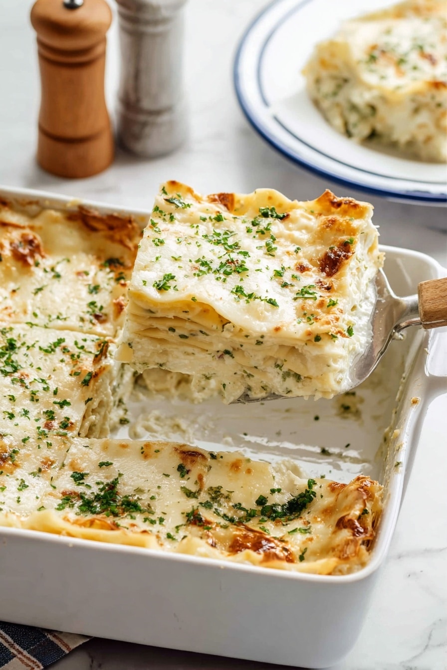 The image shows a white baking dish filled with a six-layer lasagna. Each layer consists of creamy white sauce and pasta sheets with soft, textured edges. The top layer is covered with melted white cheese sprinkled with finely chopped green herbs. The lasagna has a golden-brown crust on some edges. A metal spatula with a wooden handle is placed inside the dish, lifting one square piece from the corner. In the background, a slice of lasagna sits on a white plate with blue trim on a white marbled surface, with a blurred salt and pepper shaker set partly visible. Photo taken with an iphone --ar 2:3 --v 7 - Creamy Chicken Alfredo Lasagna, Chicken Alfredo lasagna, Creamy lasagna with chicken, Easy chicken lasagna recipe, Gourmet chicken Alfredo dish