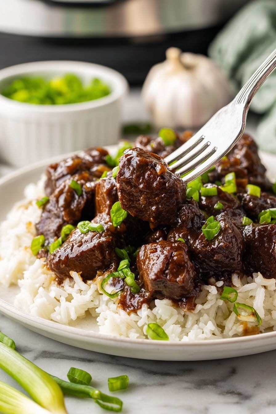 The dish shows a single white plate on a white marbled table, holding two main layers: the bottom layer is white rice with some chopped green onions scattered on top, and the top layer is dark brown beef chunks covered in a shiny glaze, also garnished with green onions. A silver fork pierces one beef chunk in the center of the plate, lifting it slightly above the rest. In the background, a whole garlic bulb and a small white bowl with more green onions are partially visible, adding to the kitchen setting. Photo taken with an iphone --ar 2:3 --v 7 - Honey Garlic Steak Bites, Honey Garlic Steak Bites Recipe, Easy Steak Bites with Honey and Garlic, Juicy Steak Bites, Savory Honey Garlic Steak Bites