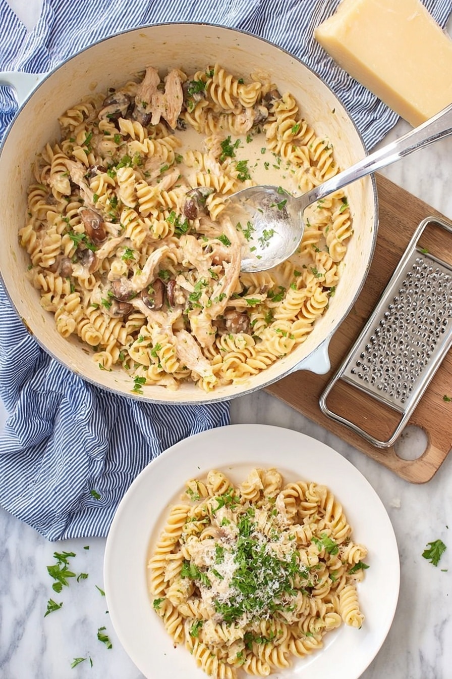 A white pot filled with creamy cooked rotini pasta mixed with light brown cooked chicken strips and small brown mushrooms, sprinkled with fresh green chopped herbs on top, a silver spoon rests inside the pot lifting some pasta. Below the pot, there is a white plate with a serving of the same pasta topped with more green herbs and a light sprinkle of grated cheese. To the side, a block of light yellow cheese and a metal grater rest on a blue striped cloth, all placed on a white marbled surface. photo taken with an iphone --ar 2:3 --v 7 - Creamy Turkey Pasta, easy Thanksgiving leftovers dinner, comforting pasta with turkey, quick turkey pasta recipe, rich creamy pasta dish