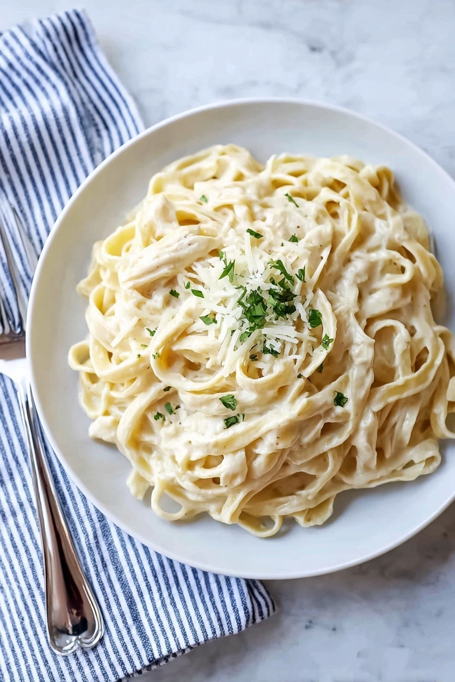 A white plate filled with a large serving of creamy fettuccine pasta, with smooth, thick noodles coated in a pale, off-white sauce. On top in the center, there is a small pile of grated white cheese and finely chopped green herbs adding a touch of color. The dish sits on a white marbled surface, with a silver fork resting on a striped blue and white cloth to the left side of the plate. The lighting is soft and natural, highlighting the creamy texture of the pasta and the freshness of the garnish. photo taken with an iphone --ar 2:3 --v 7 - Creamy Fettuccine Alfredo, creamy pasta recipe, homemade Alfredo sauce, easy Italian pasta, quick weeknight dinner