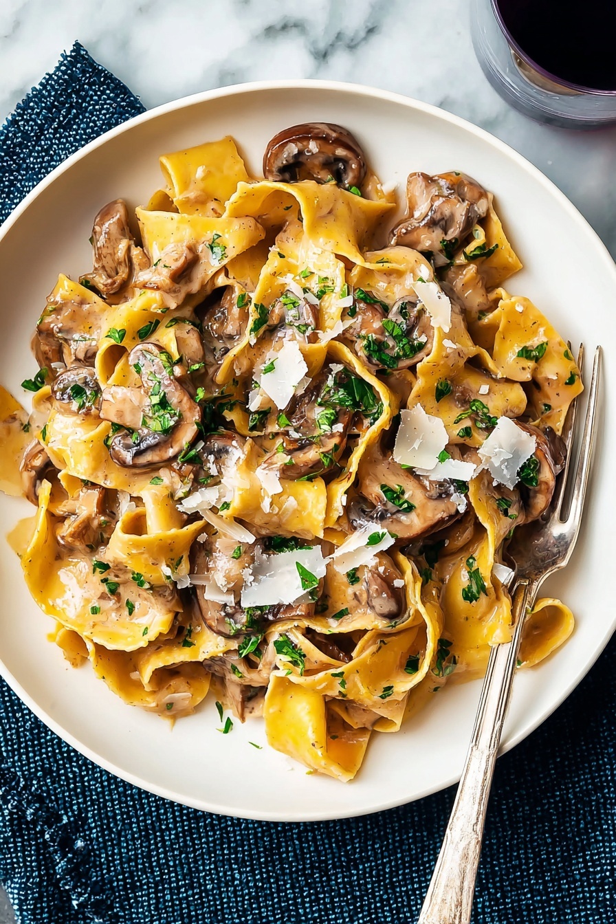 A white plate holds a serving of wide, yellow pasta ribbons cooked in a light brown creamy mushroom sauce. On top, there are several brown, slightly browned mushroom slices mixed throughout the pasta, adding a smooth texture. Bright green chopped herbs are sprinkled over the dish, giving a fresh contrast. Light shavings of white cheese are scattered on top, melting slightly into the sauce. A silver fork rests on the edge of the plate, and the plate is placed on a white marbled surface with a dark blue textured cloth beneath one side. Photo taken with an iphone --ar 2:3 --v 7 - Creamy Vegetarian Mushroom Stroganoff, vegetarian mushroom steak, quick mushroom dinner, vegan mushroom sauce, easy vegetarian mushroom recipes
