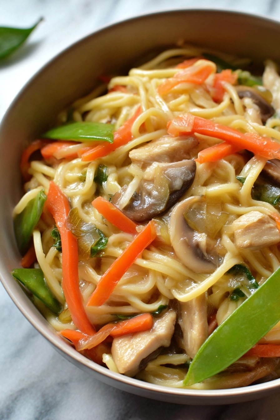 A close-up shot of a round white bowl filled with a noodle dish that has three main visible layers. The base layer consists of light yellow noodles that look soft and slightly shiny. Mixed in and on top of the noodles are bright orange thin carrot strips, pale green sliced snow peas, and light brown sliced mushrooms. Scattered throughout are small pieces of light brown cooked chicken or tofu, adding texture contrast. The background shows an out-of-focus white marbled surface, giving the dish a clean and fresh look. Photo taken with an iphone --ar 2:3 --v 7 - Instant Pot Chicken Lo Mein, easy chicken lo mein, healthy chicken noodle stir-fry, quick weeknight dinner recipes, one-pot lo mein