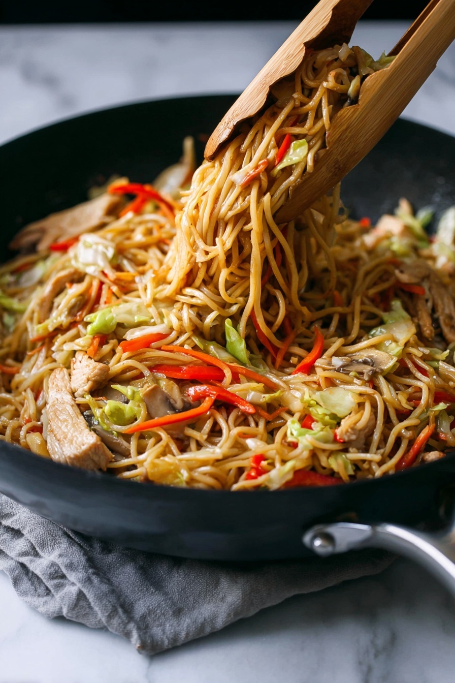 A close-up of a black skillet filled with cooked stir-fried noodles lifted by wooden tongs, showing three main layers: a base layer of thin, light brown noodles tangled together; mixed throughout are slices of light beige cooked meat and strips of vegetables including red bell peppers, pale green cabbage, thin orange carrot sticks, and light brown mushrooms. The noodles have a slightly shiny texture, and the colors of the vegetables add bright, fresh contrast. The skillet rests on a white marbled surface with a subtle grey cloth partially visible under the handle. photo taken with an iphone --ar 2:3 --v 7 - Chicken Yakisoba Stir-Fry, Chicken Yakisoba, Japanese stir-fry recipes, easy chicken stir-fry, quick Asian noodle dishes