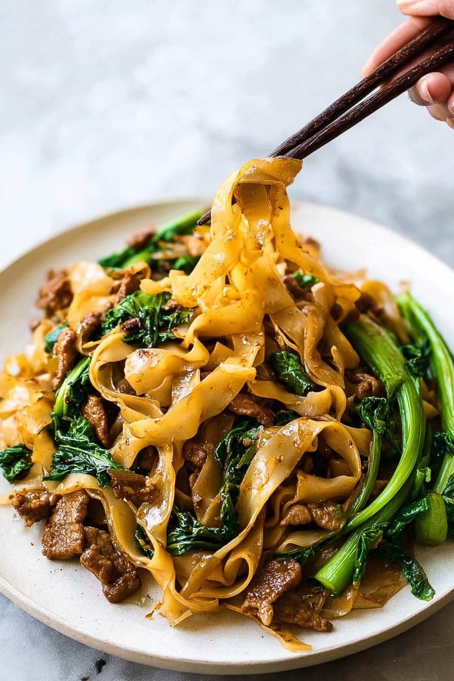 This image shows a white plate filled with wide flat light brown noodles mixed with small pieces of browned meat and bright green leafy vegetables. The noodles look soft and slightly oily, hanging in strands from dark brown chopsticks held by a woman's hand. The meat pieces are scattered throughout the dish, with some near the edges and some under the noodles. The green vegetables add a fresh look, with stems and leaves placed mostly on the right side of the plate. The background is a soft white marbled texture, keeping the focus on the colorful noodles and greens. Photo taken with an iphone --ar 2:3 --v 7 - Easy Thai Pad See Ew Stir Fry, Thai Pad See Ew, Stir Fry recipes, Thai street food, quick Asian noodle dishes