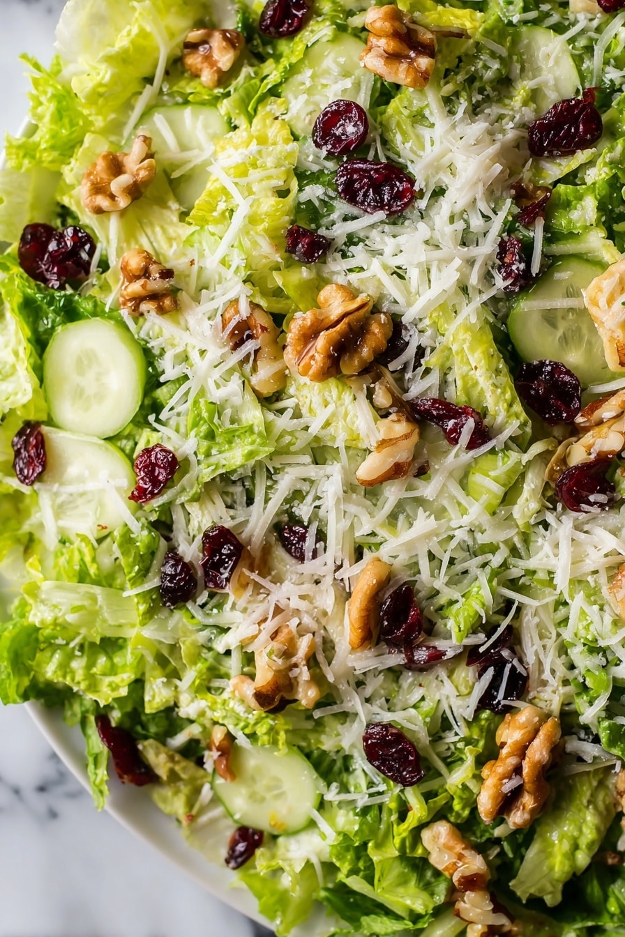 The image shows a close-up view of a fresh salad with several layers. The base layer consists of thinly shredded bright green lettuce. Scattered on top are thin slices of pale green cucumber, adding a smooth texture. There are pieces of light brown walnuts sprinkled across, giving a rough, chunky look. Interspersed are small dark red dried cranberries providing contrasting color and texture. The final layer is a light dusting of white shredded cheese spread evenly over the top. The salad is on a white plate placed over a white marbled surface. photo taken with an iphone --ar 2:3 --v 7 - Brussels Sprouts Apple Cranberry Salad, healthy holiday salad, easy Brussels sprouts salad, fall veggie salad with cranberries, quick festive salad