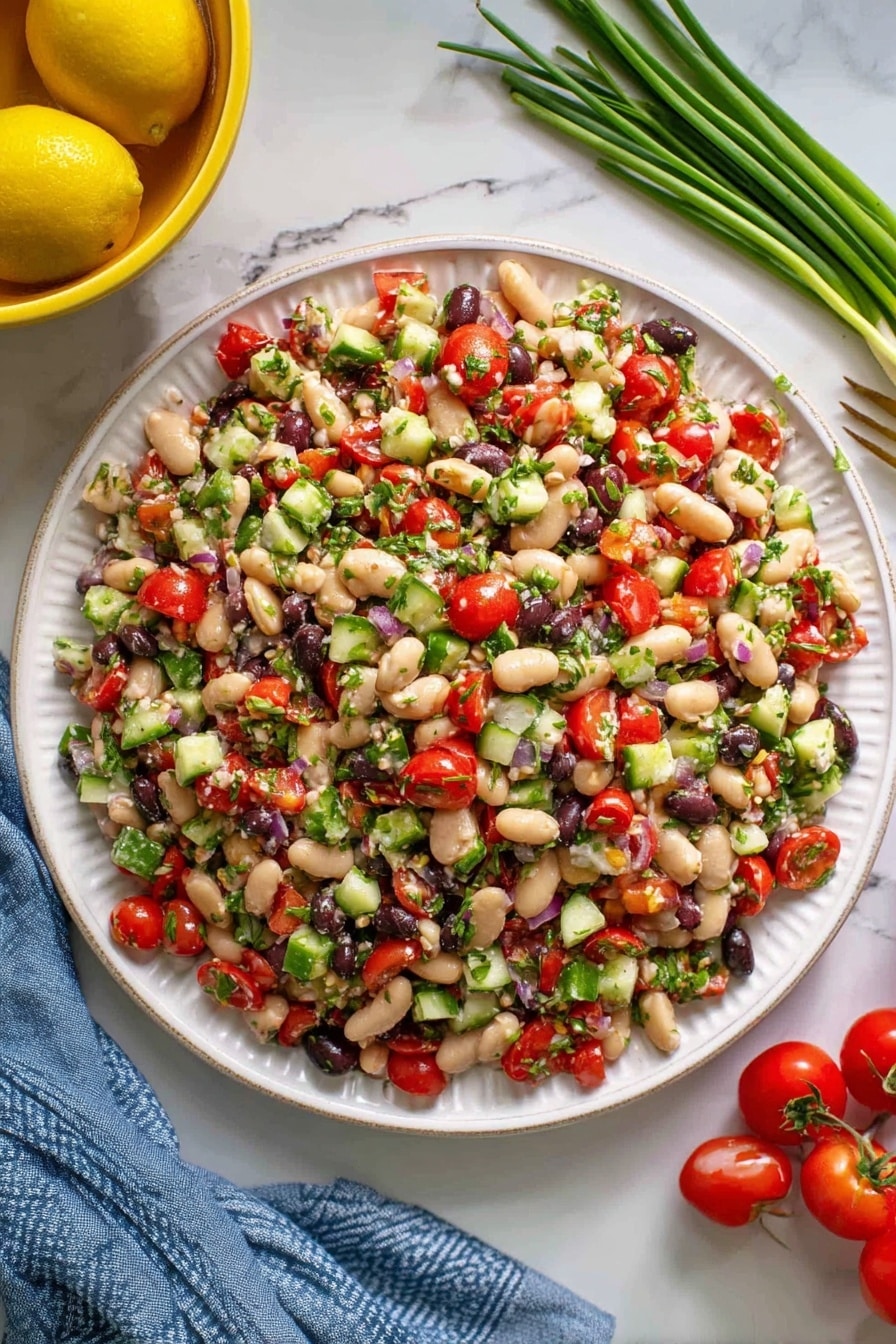 A white plate is filled with a colorful bean salad that has many small chopped pieces. The salad has white beans, red cherry tomato pieces, small green cucumber chunks, black beans, and bits of green herbs evenly spread on top. The texture looks fresh and slightly moist, mixed but not mushy. Around the plate, there are whole cherry tomatoes to the right, some green onions laying on a white marbled surface in the upper right, and a yellow bowl with lemons in the upper left. A blue cloth is partially visible under the plate. Photo taken with an iphone --ar 2:3 --v 7 - Mediterranean Bean Salad with Feta, healthy bean salad, easy Mediterranean salad, vegetarian bean salad, quick summer salad