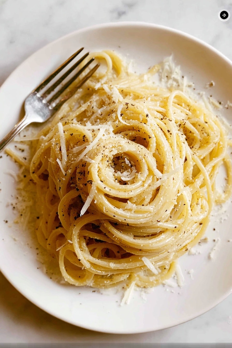 A white round plate holds a neatly twirled mound of spaghetti pasta as the main layer, pale yellow in color with a slight shine. Scattered over the pasta are small, irregular shreds of white cheese that add texture and light contrast to the smooth noodles. Black pepper flakes are sprinkled lightly, creating small dark spots across the dish. To the left side of the plate, a silver fork is partially visible, resting beside the pasta. The background has a white marbled texture, creating a clean and simple setting. Photo taken with an iphone --ar 2:3 --v 7 - Creamy Cacio e Pepe Pasta, Cacio e Pepe pasta recipe, how to make creamy cacio e pepe, easy cacio e pepe pasta, quick Italian pasta dish