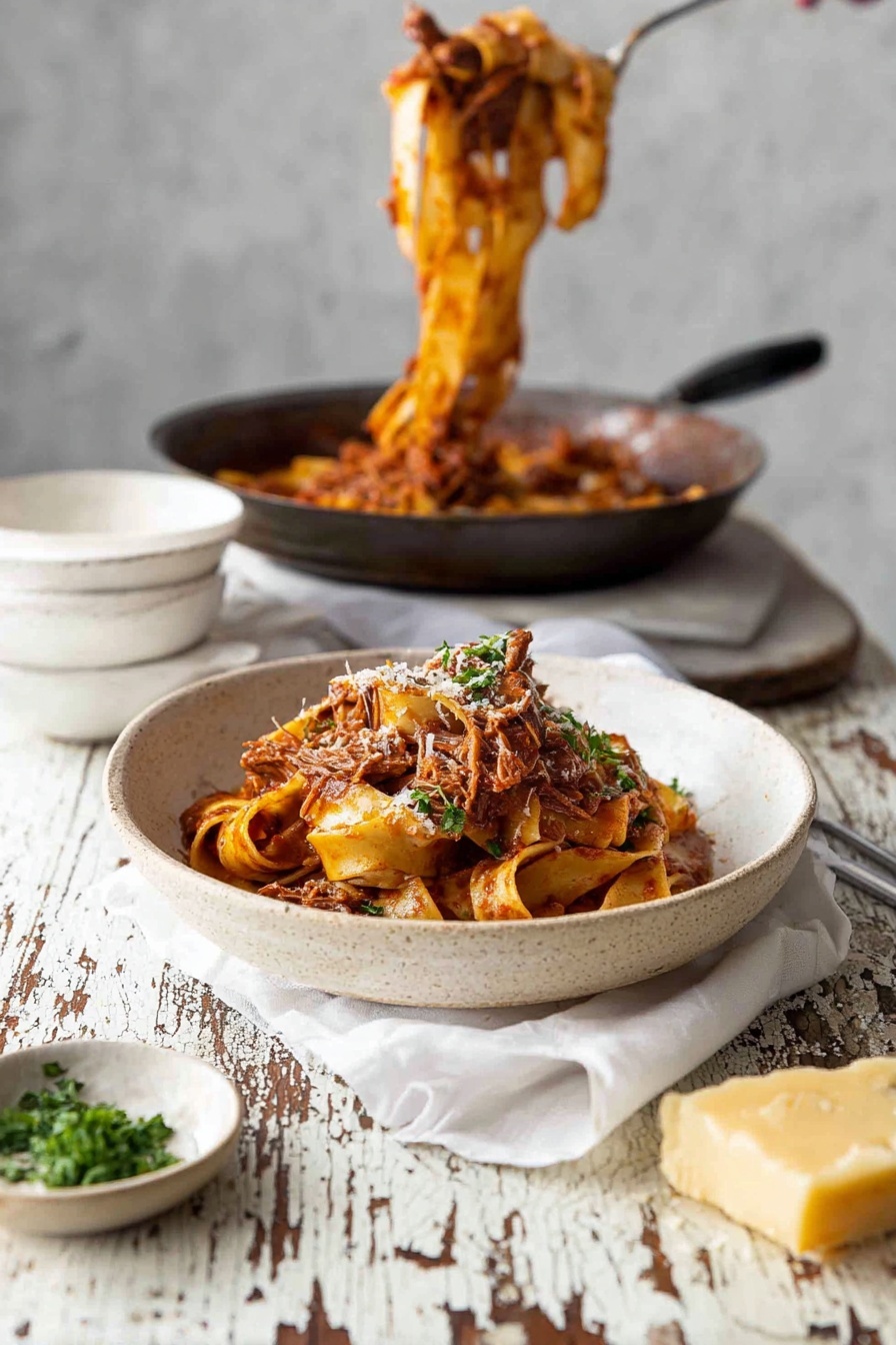 A white bowl with a rough texture holds several layers of wide flat pasta ribbons in a reddish-brown tomato sauce mixed with shredded meat, topped with green parsley and a sprinkle of grated cheese. Behind it, a dark pan contains more pasta in sauce being lifted upwards, while an empty white bowl rests on a white cloth on a worn white marbled table with chipped paint. To the left of the bowl is a small dish of chopped green herbs, and at the bottom right a grater with a chunk of yellow cheese sits on the table. The scene is light and rustic, photo taken with an iphone --ar 2:3 --v 7 - Slow Cooked Beef Ragu with Pasta, Italian Beef Ragu, Easy Beef Ragu Recipe, Comforting Pasta Dish, Slow Cooker Beef Pasta
