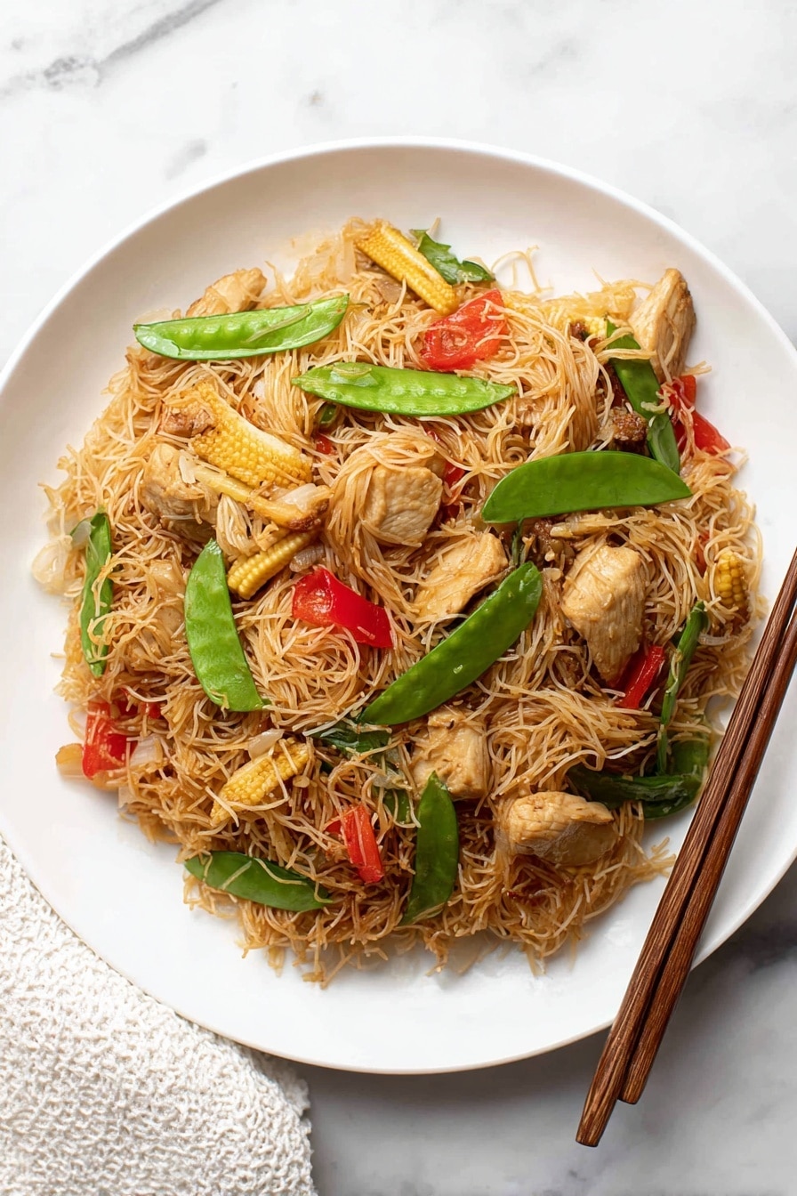 The dish shows a single layer of thin brown rice noodles mixed with pieces of light brown cooked chicken, small baby corn slices, bright green snap peas, red bell pepper slices, and bits of translucent cooked onion on a white plate. The plate is placed on a white marbled surface. To the right of the plate, there are two brown wooden chopsticks resting diagonally. A white textured cloth is partially visible at the bottom left corner of the image. photo taken with an iphone --ar 2:3 --v 7 - Singapore Curry Noodles, easy Singapore curry noodles, Asian noodle recipes, quick curry noodle dish, flavorful noodle recipes