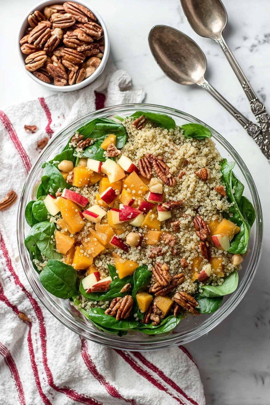 This image shows a clear glass bowl filled with a colorful quinoa salad. The base layer is light, fluffy quinoa with small, round grains scattered evenly throughout. Mixed inside are bright green fresh spinach leaves with a smooth texture, orange chunks of butternut squash, and small pale beans adding softness. Red-skinned apple pieces give a splash of red color, and whole pecans add a textured, brown, nutty layer randomly placed on top. The bowl is on a white marbled surface with a soft striped cloth nearby, and a woman's hand holds a dark metal salad spoon at the edge. photo taken with an iphone --ar 2:3 --v 7 - Roasted Butternut Squash Quinoa Salad, healthy roasted squash salad, quinoa vegetable salad, seasonal fall salads, nutritious vegetarian salads