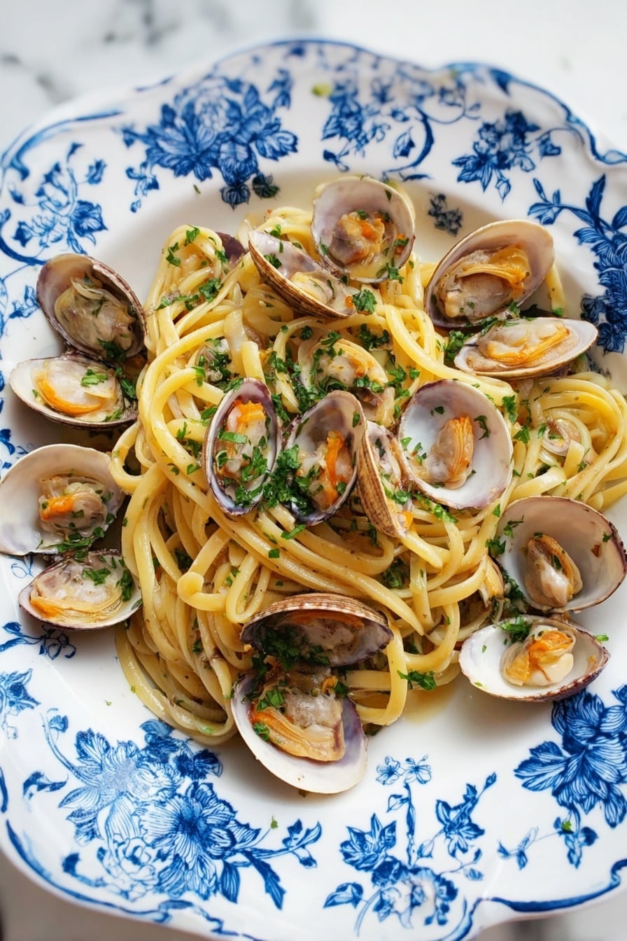 A white plate with blue floral patterns holds a serving of spaghetti pasta as the bottom layer, light yellow and slightly shiny. On top of the pasta, there are many open clam shells with light brown and white inner textures and soft orange clam meat inside. The dish is sprinkled with finely chopped green parsley evenly over the pasta and clams. The plate is placed on a white marbled surface. photo taken with an iphone --ar 2:3 --v 7 - Linguine with Clams, clam linguine recipe, Italian pasta with clams, easy seafood pasta, briny garlic pasta